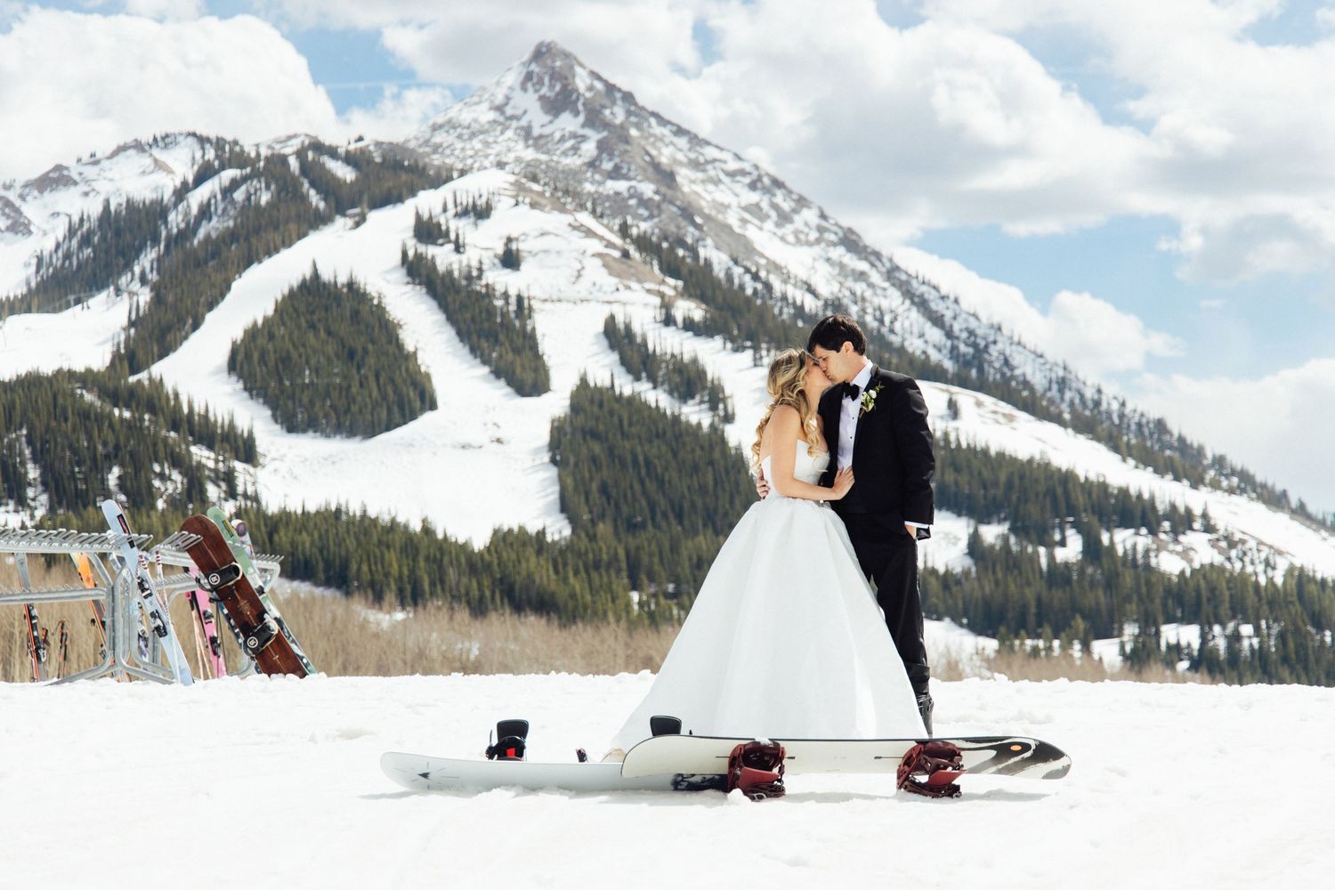 Bride and groom kissing on a snowboard with snowy mountain backdrop at a winter wedding in Colorado.