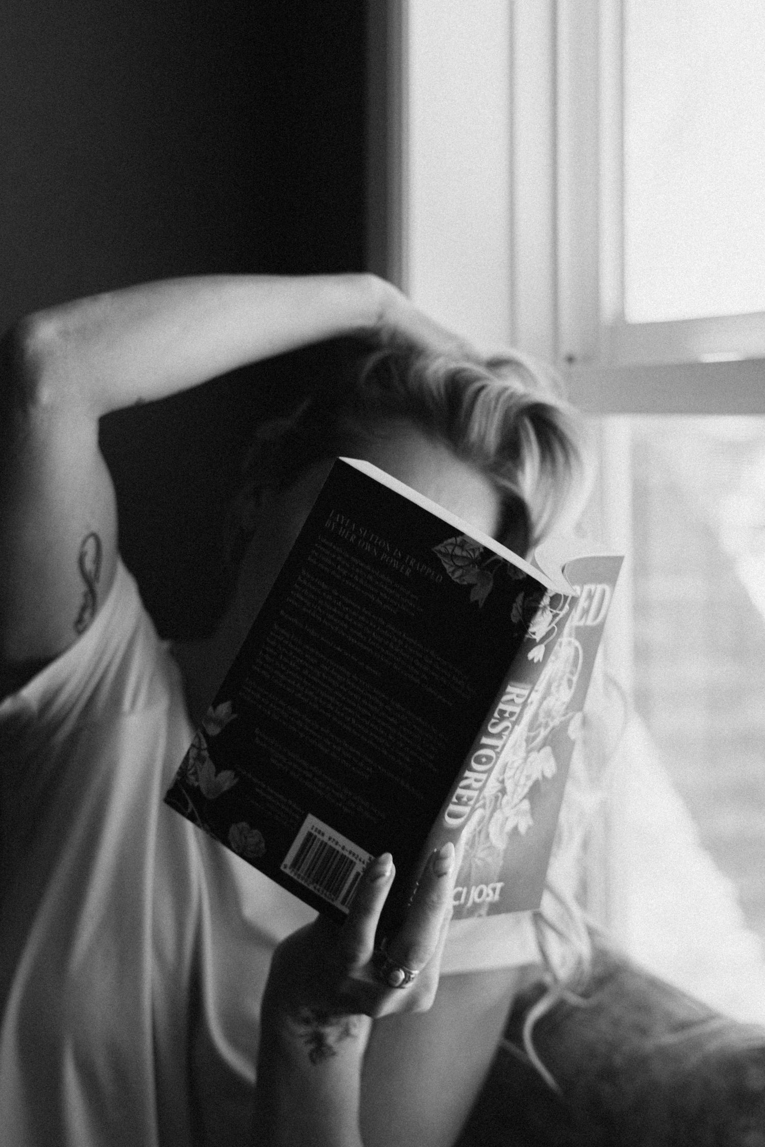 Person reading book in dramatic black and white window lighting.