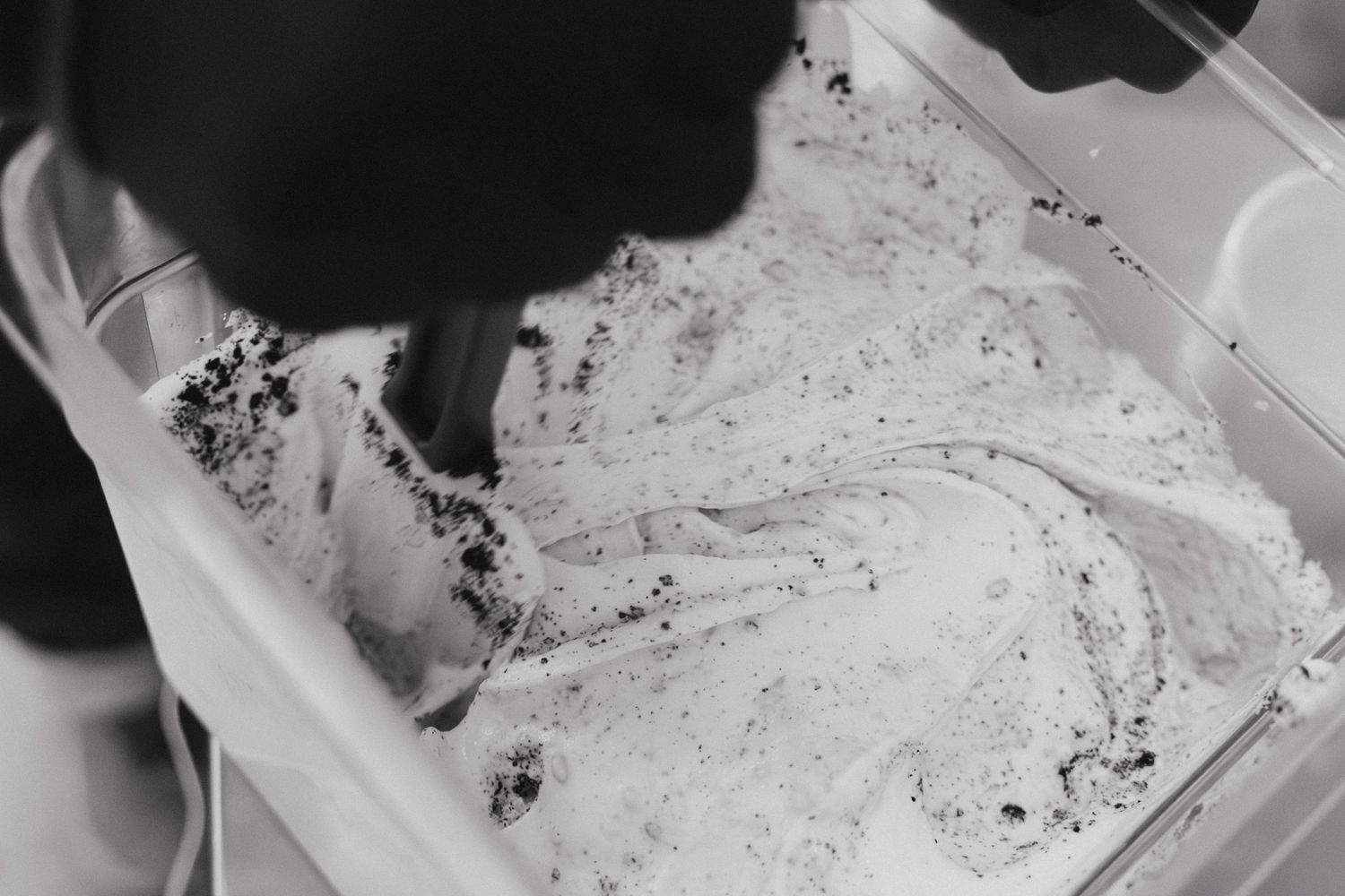 Black and white close-up of creamy ice cream with dark cookie swirls in a container.