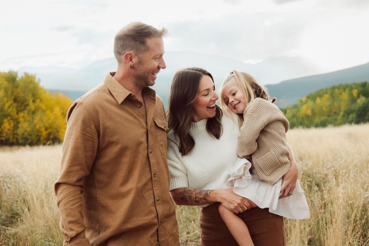 Family portrait session in a golden field with mountains visible in the background.
