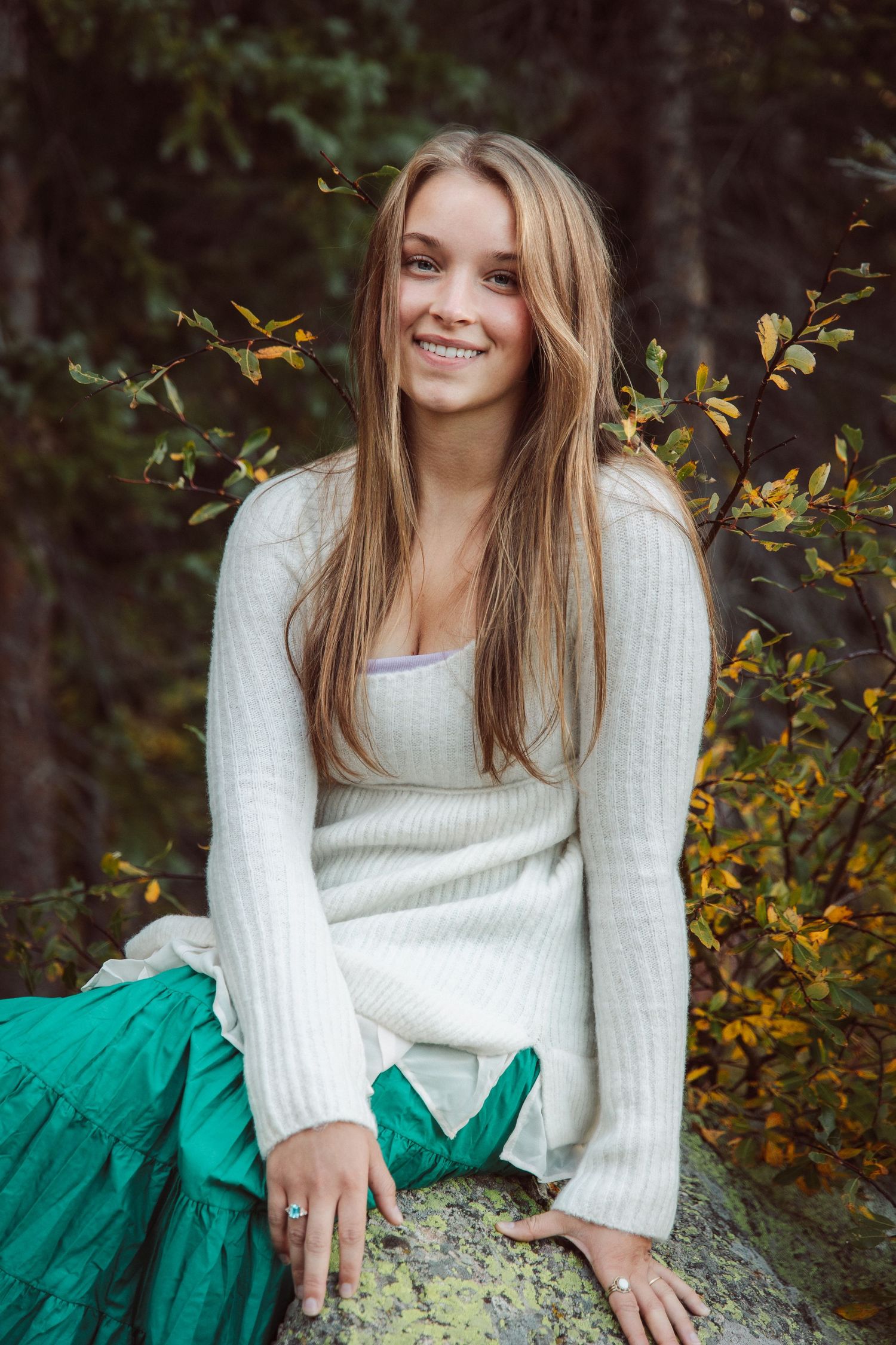 Portrait of someone in a white sweater against autumn foliage with yellow leaves.