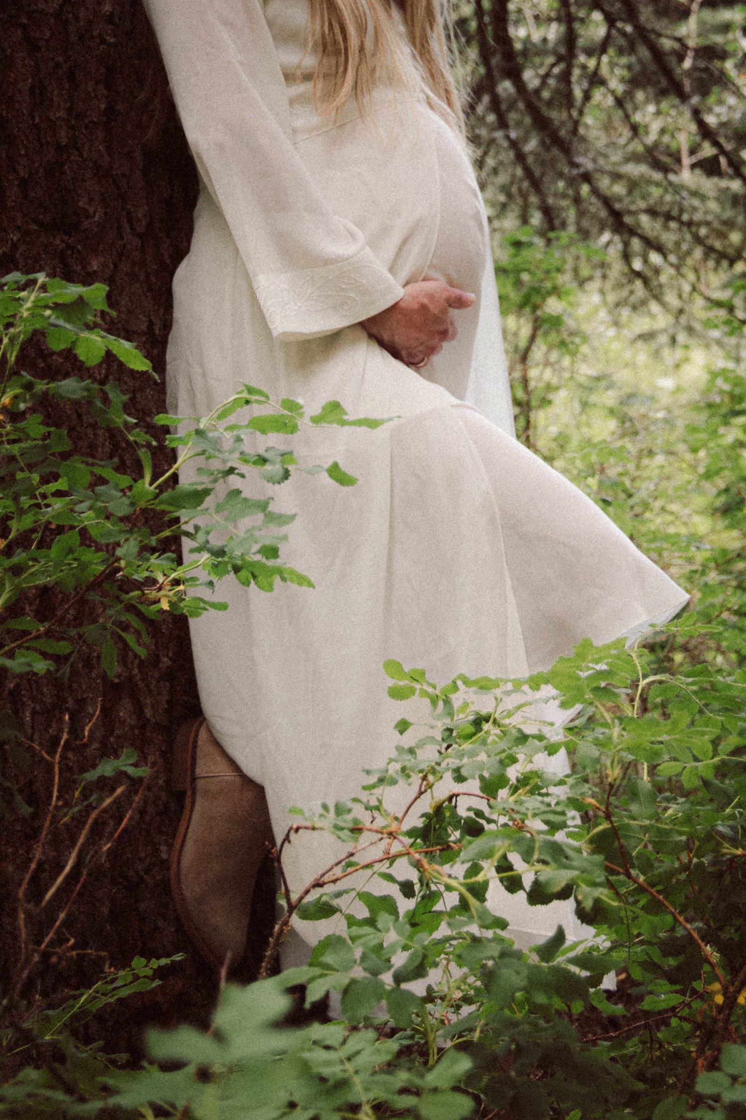 Romantic couple in white clothing embracing among green forest foliage.
