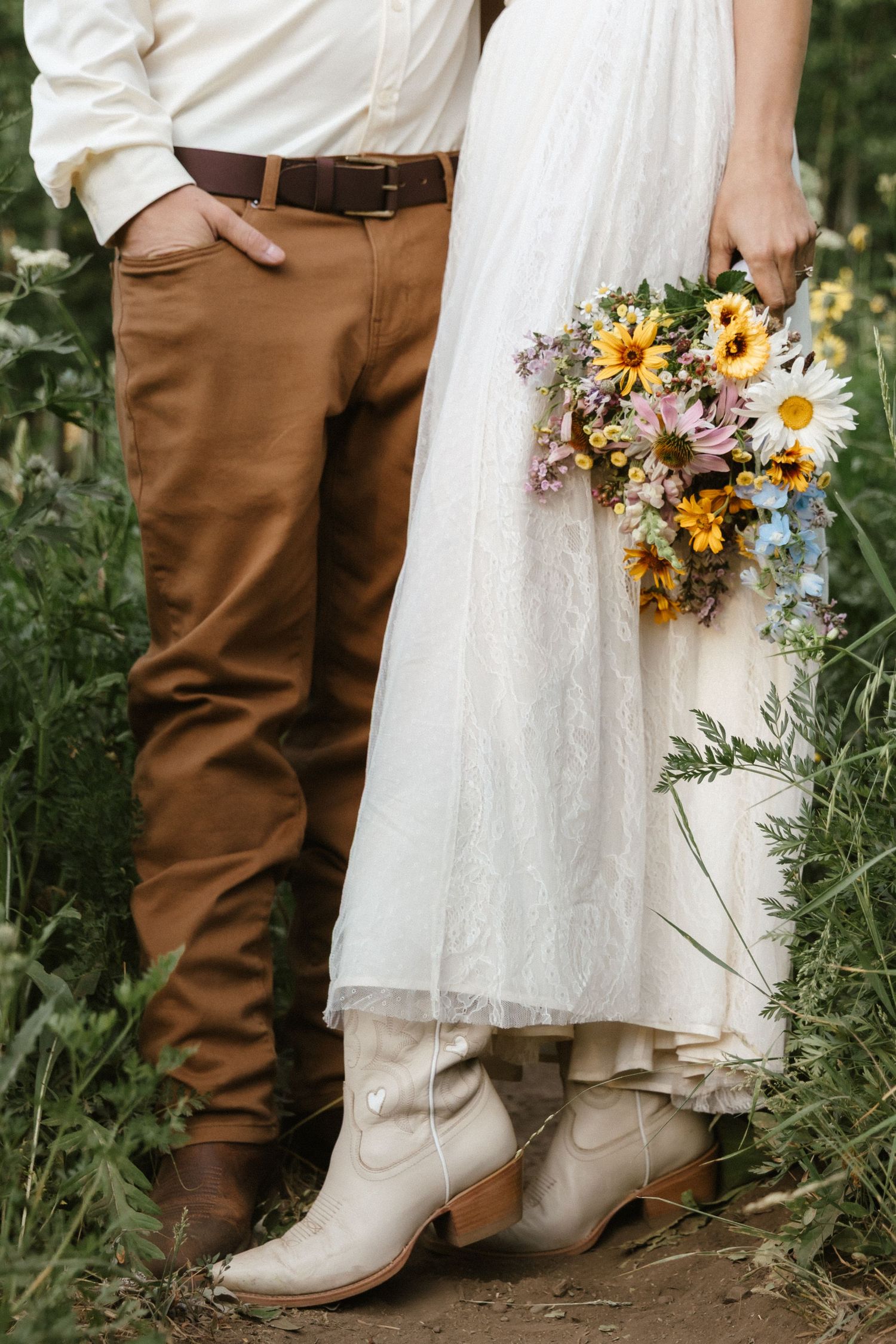 Close-up details of white boots and a floral bouquet against brown pants in an outdoor setting.