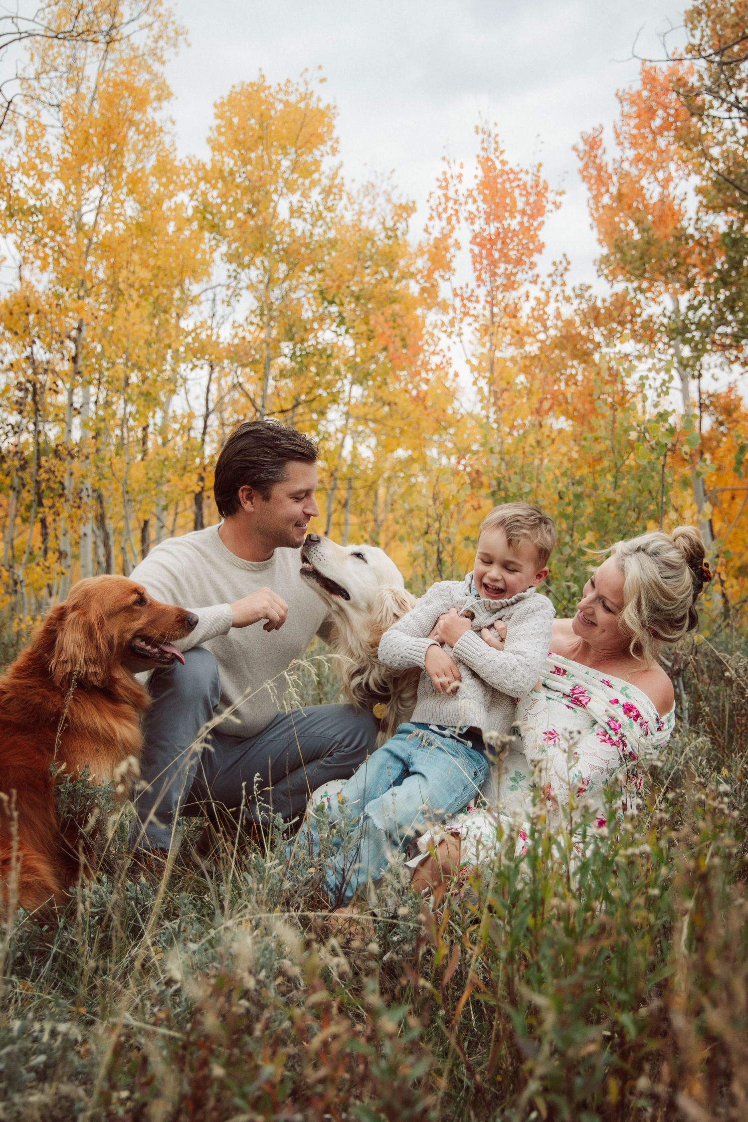 Family lying together in autumn grass with golden aspen trees in background during fall photoshoot.