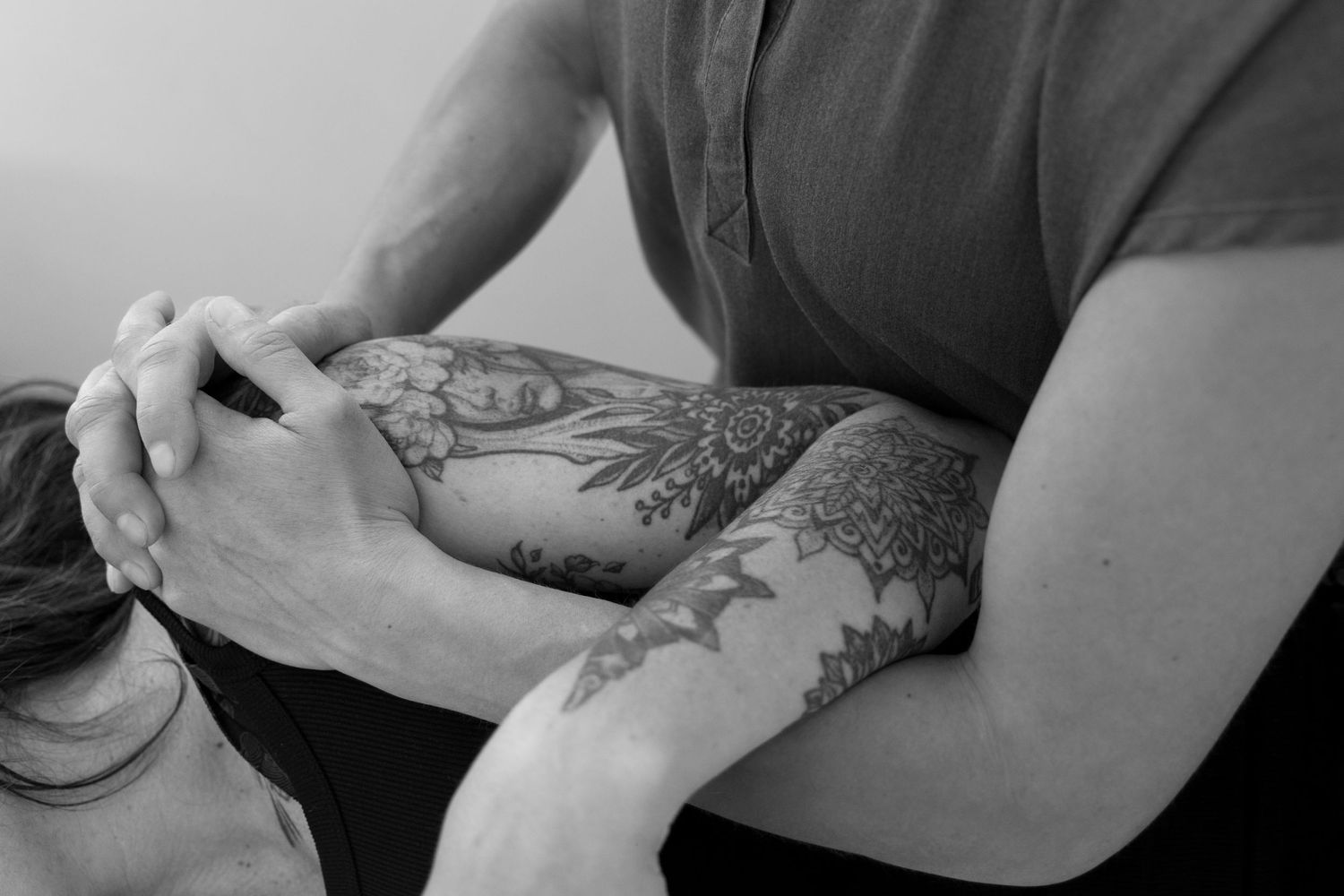 Black and white photo of a tattooed arm performing a chiropractic neck adjustment on a patient.