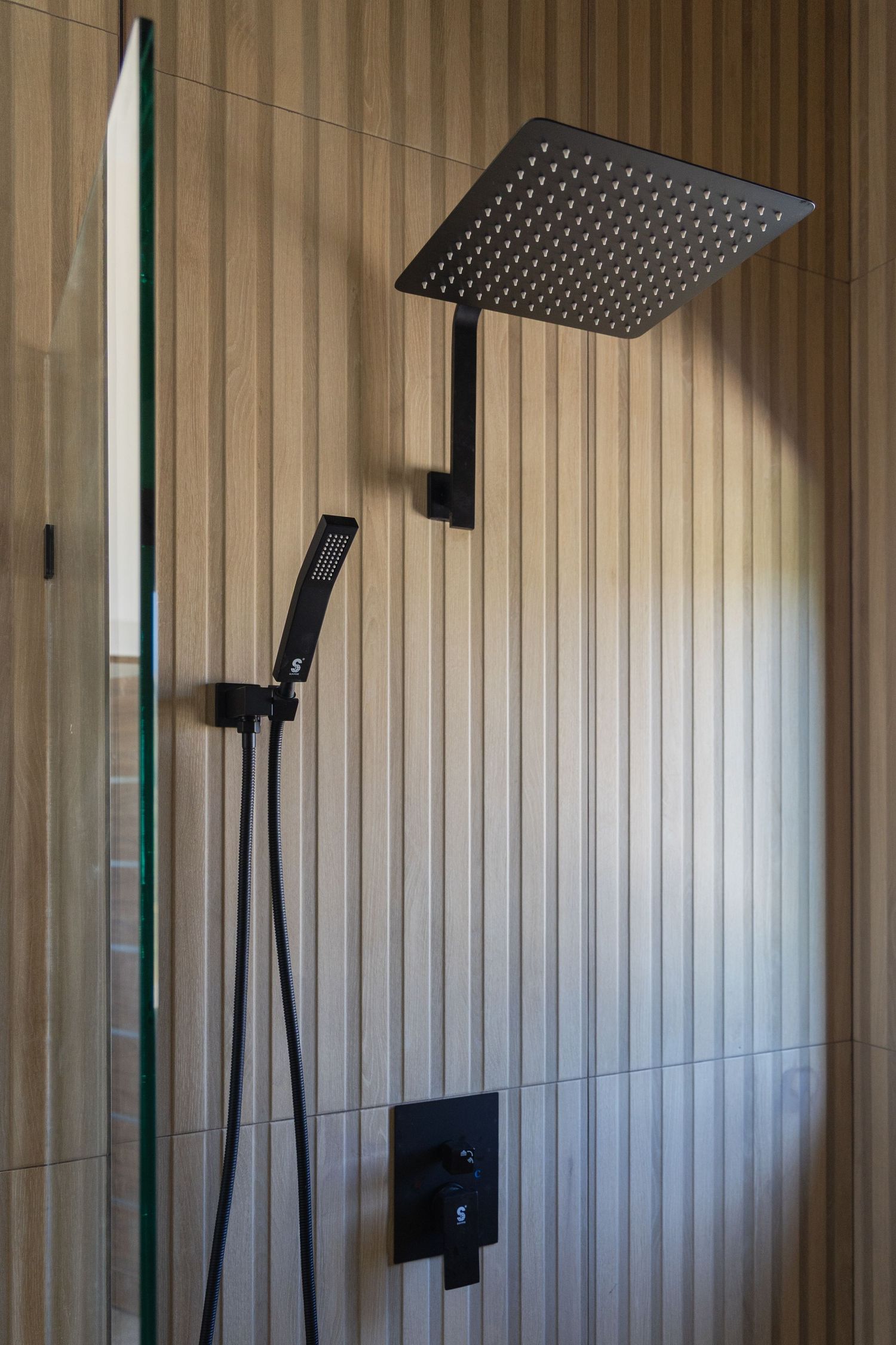 Modern black matte rain shower head and handheld fixture against ribbed wood-effect wall tiles in luxury bathroom.