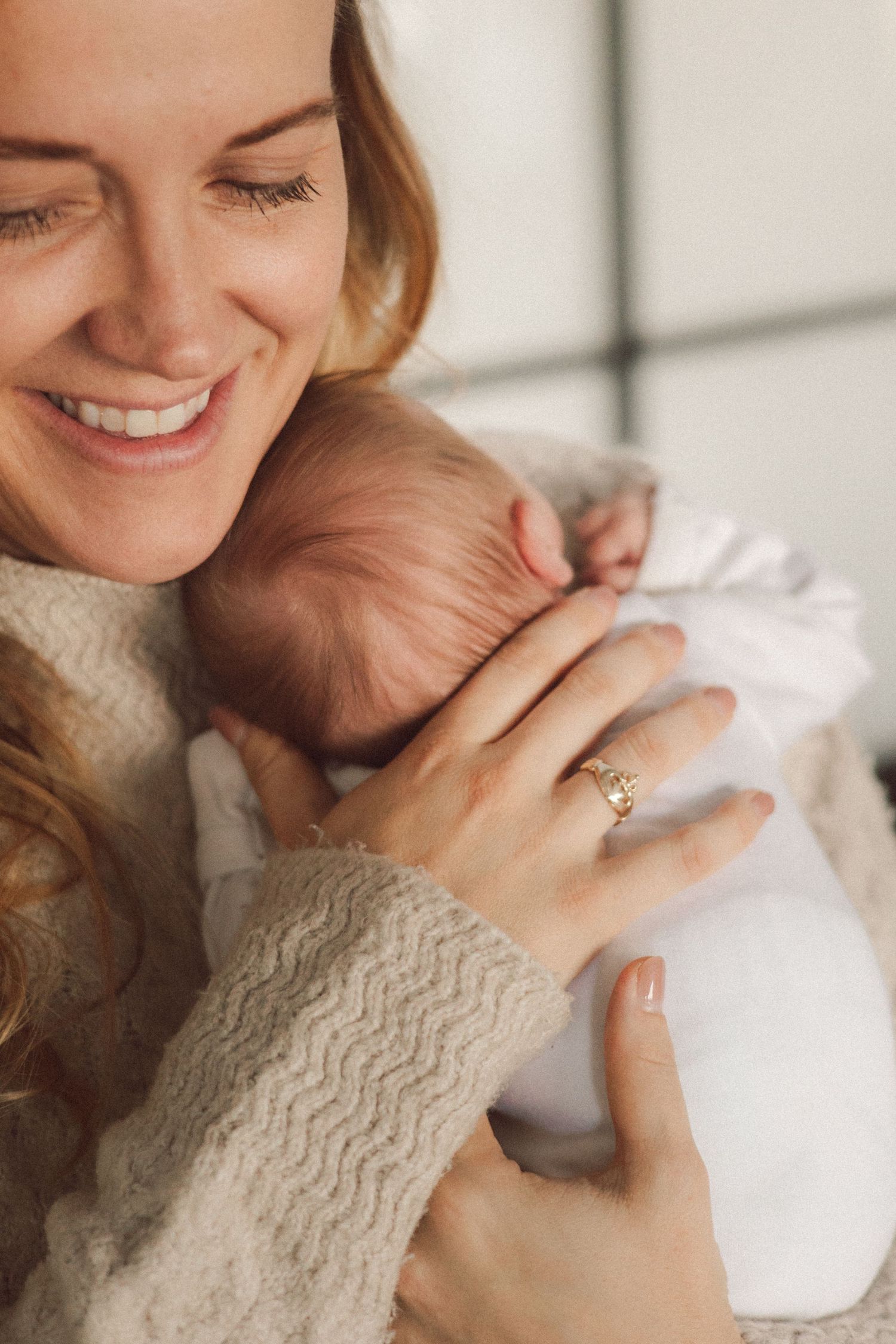A tender moment captured as a parent in a cozy sweater embraces their newborn baby wrapped in white.