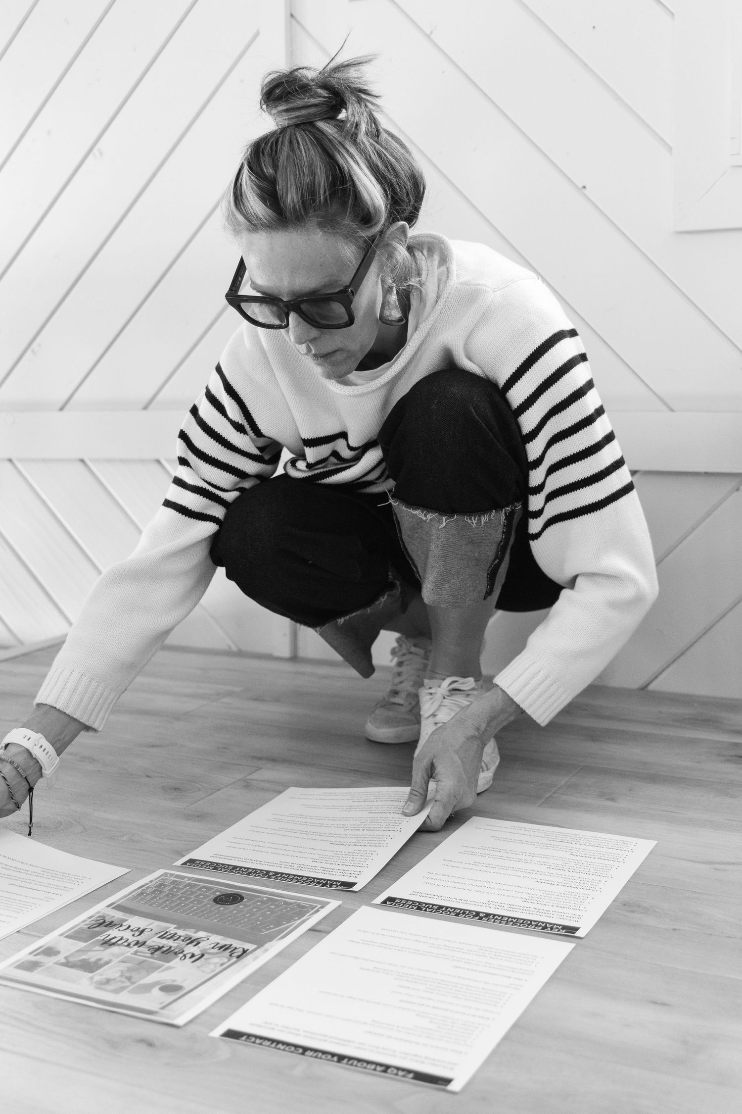 A person wearing glasses and striped shirt leans over a desk to write in a calendar or planner.
