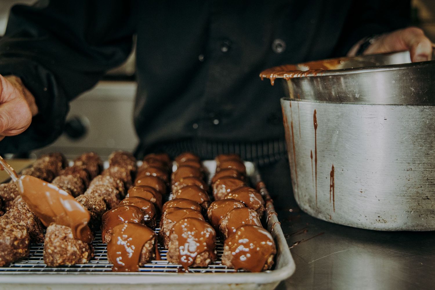 Fresh chocolate croissants cooling on metal baking sheets in a professional bakery kitchen.