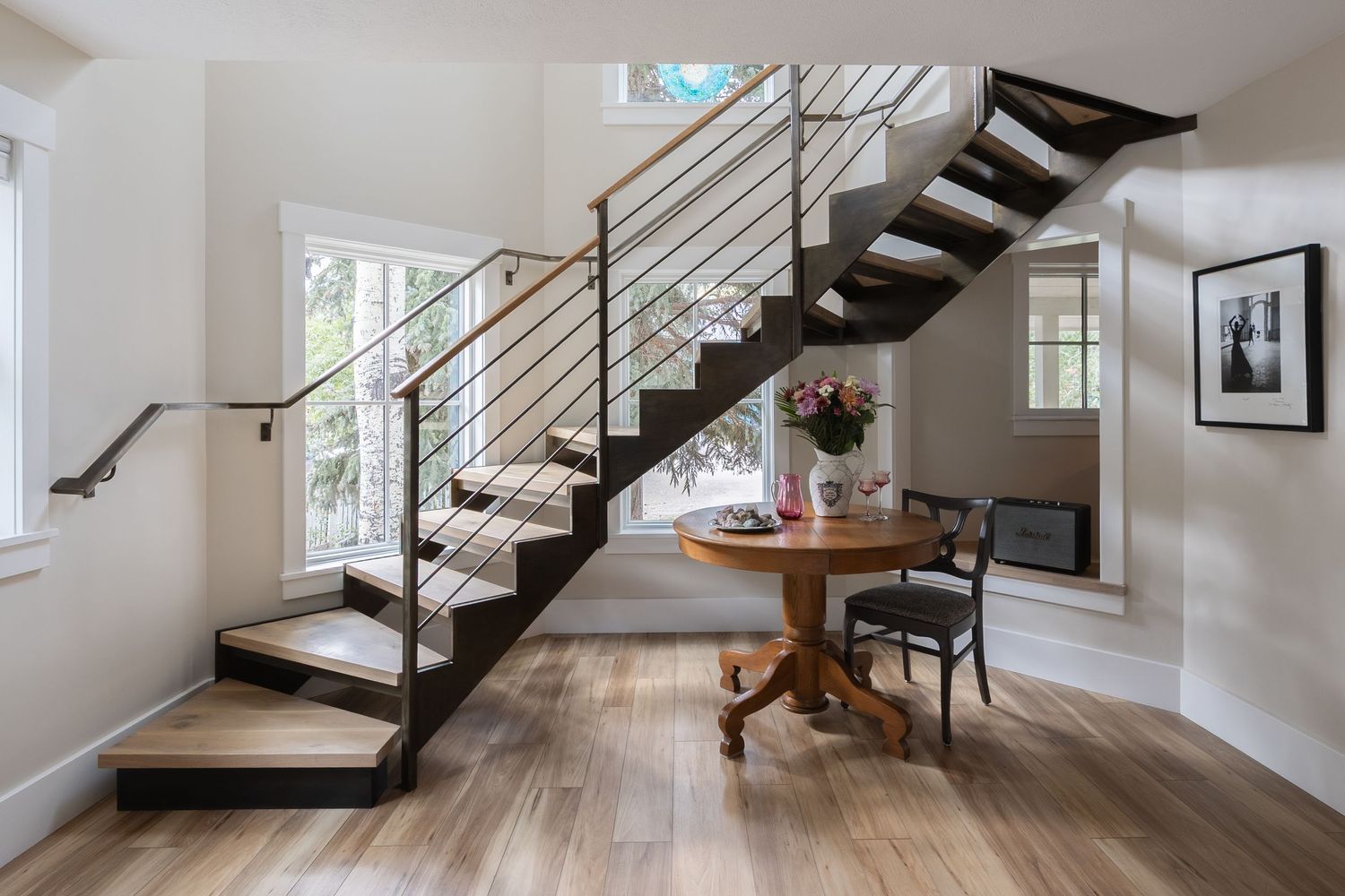 Modern staircase with dark wood steps and metal railings beside a round wooden table on hardwood floors.