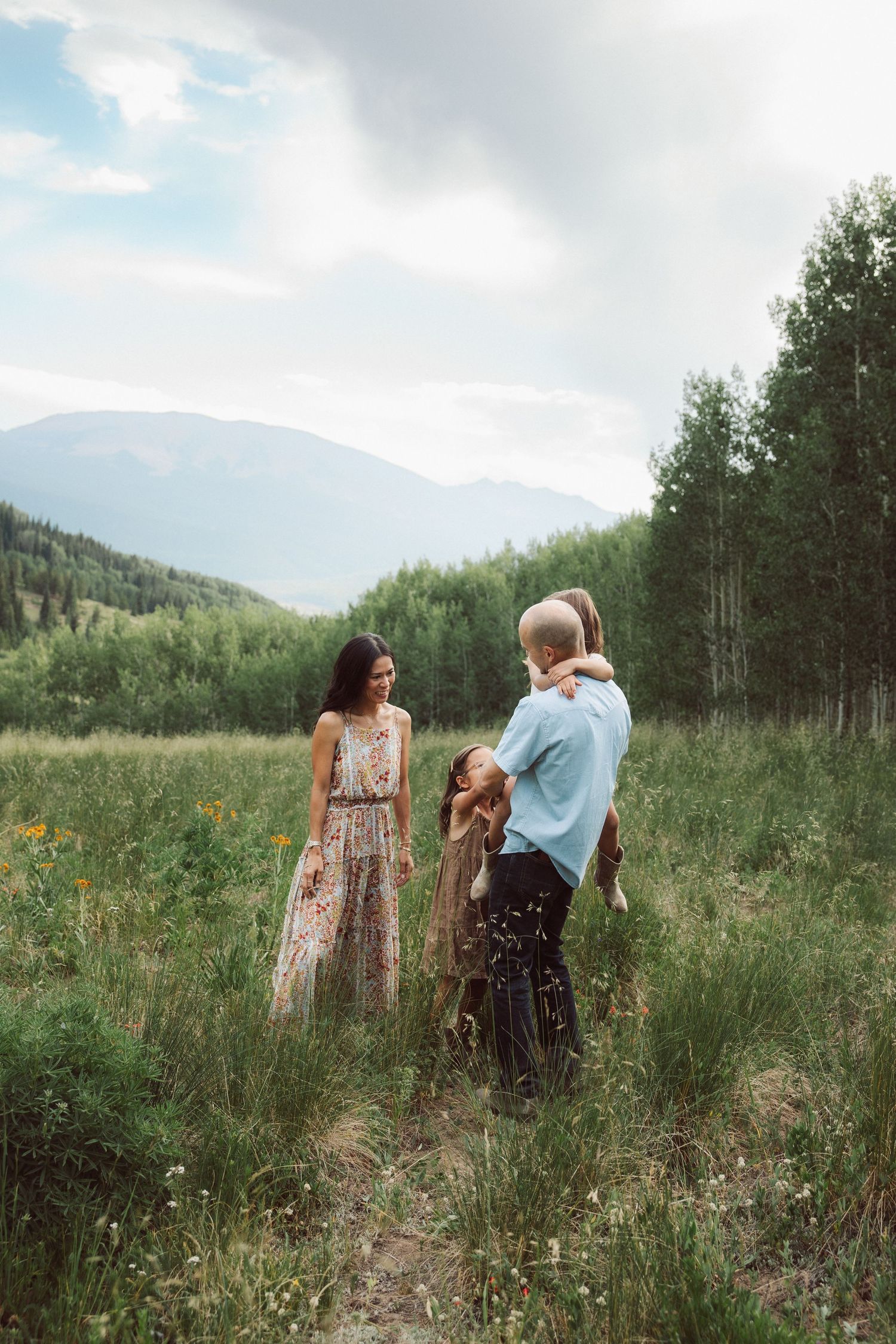 Family in a mountain meadow with wildflowers, aspen trees, and cloudy skies in a scenic Colorado landscape.