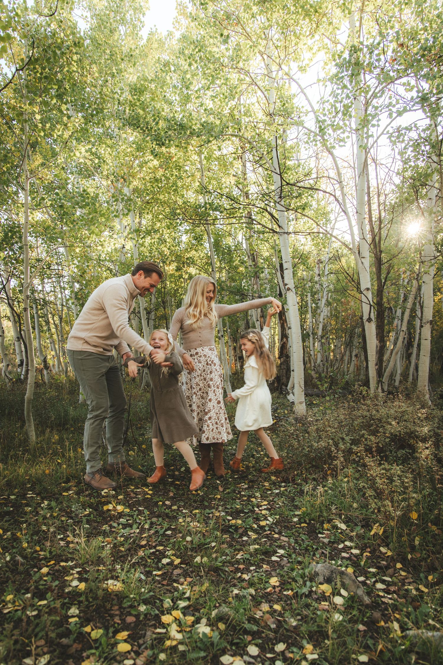 Family of four joyfully playing among white birch trees in an autumn forest with golden fallen leaves.