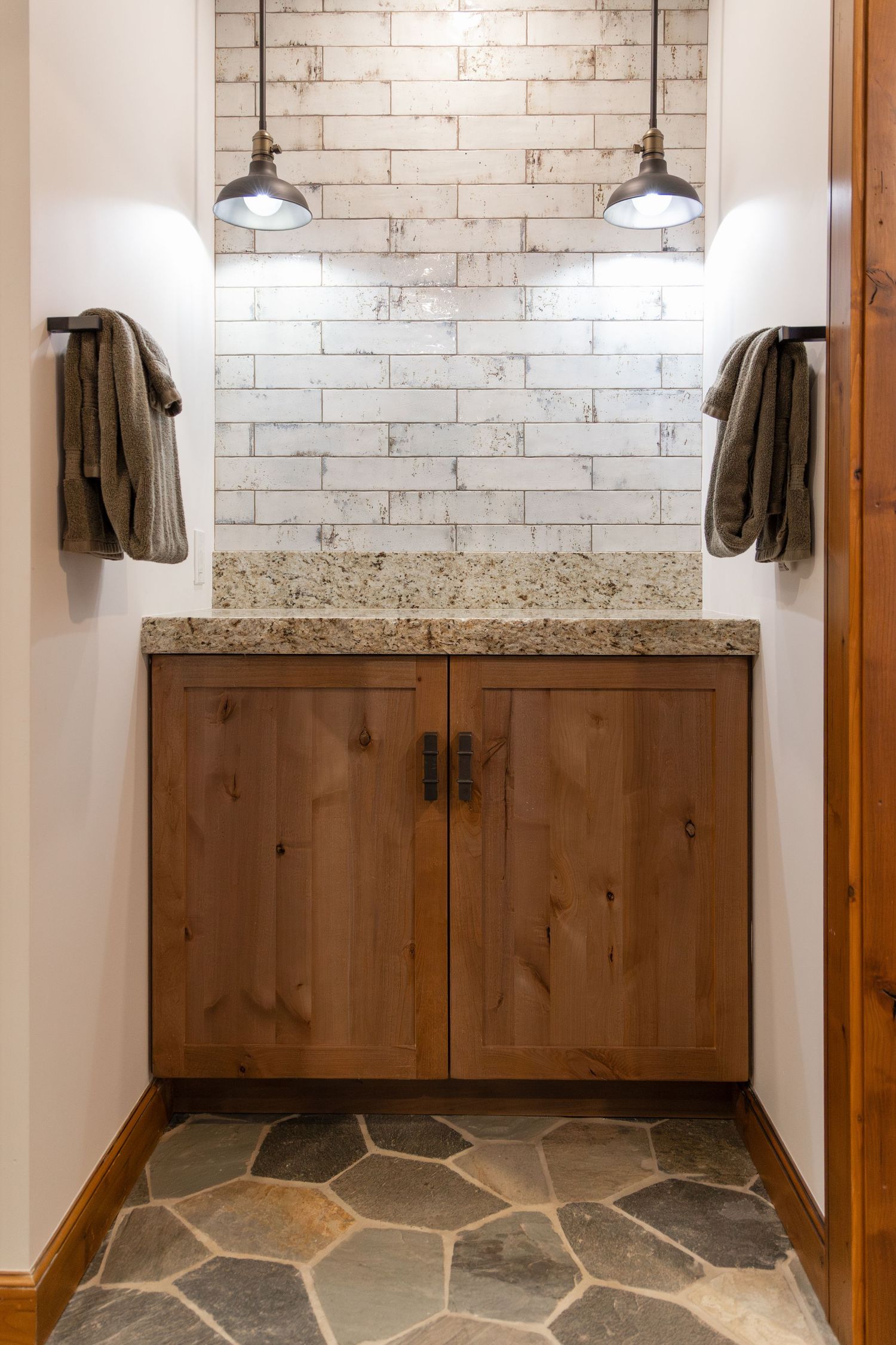 Rustic mudroom with wood cabinets, granite countertop, brick tile backsplash, pendant lights, and stone floor.