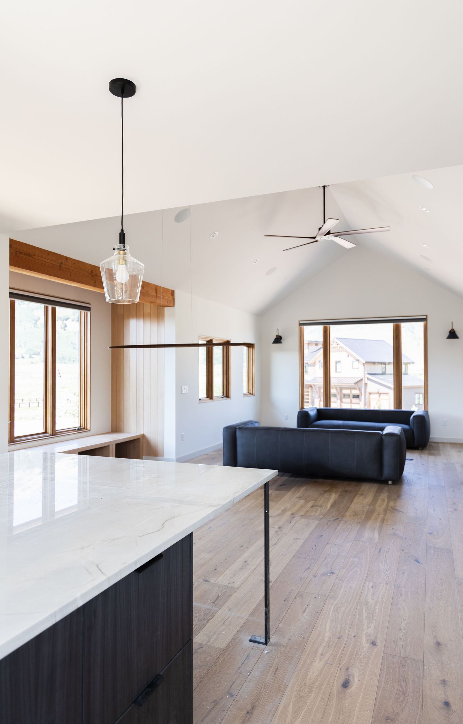 Modern open-concept kitchen and living room with vaulted ceilings, hardwood floors, marble island, and ceiling fan.