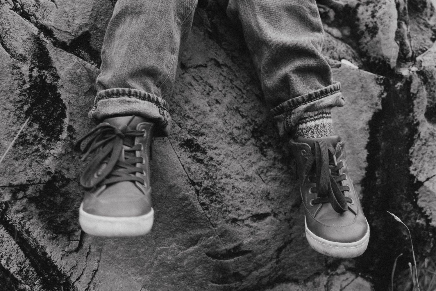 Black and white close-up of casual sneakers on rocky surface.