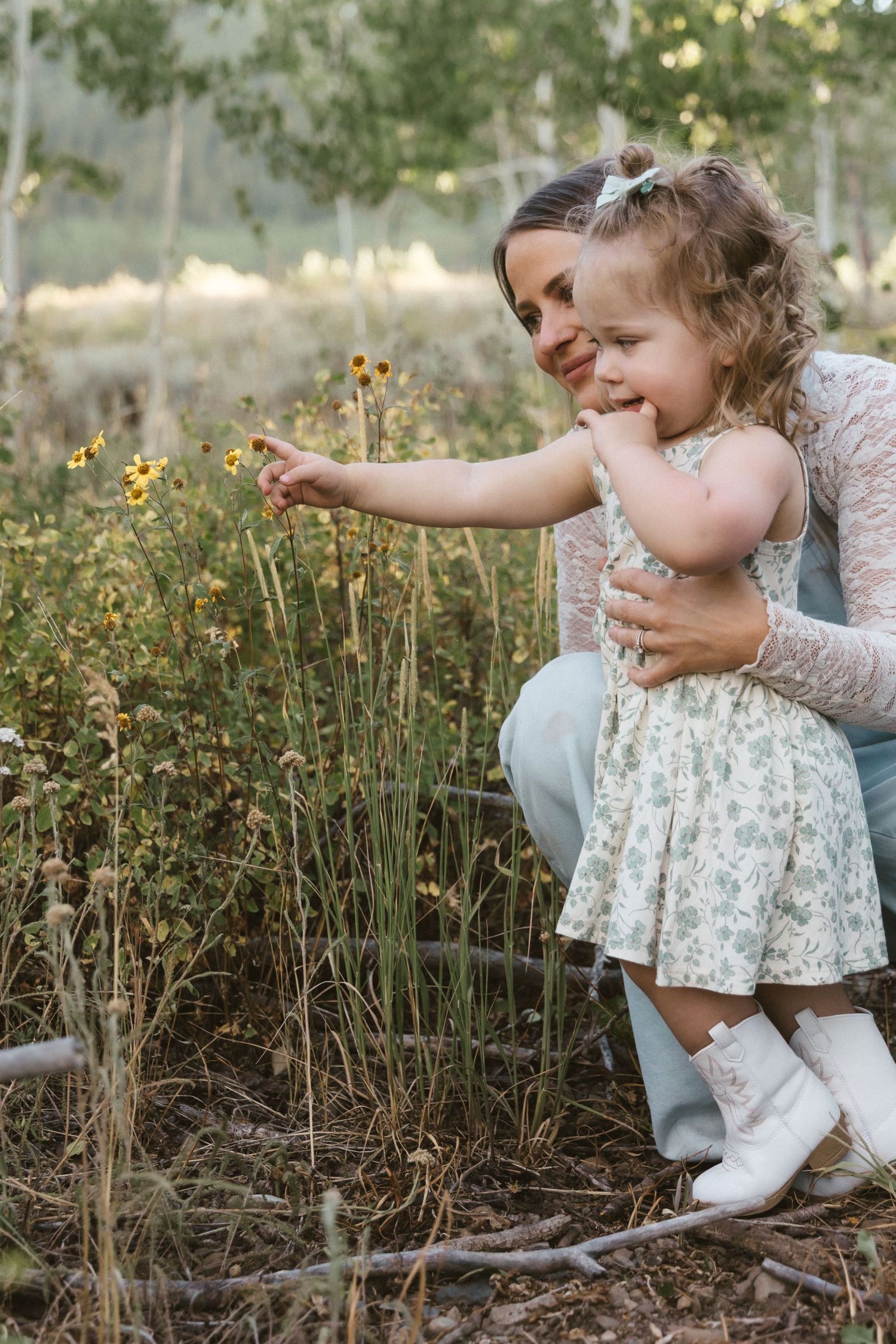 A tender moment in a wildflower field as a small child in a floral dress reaches out to touch blooming flowers.