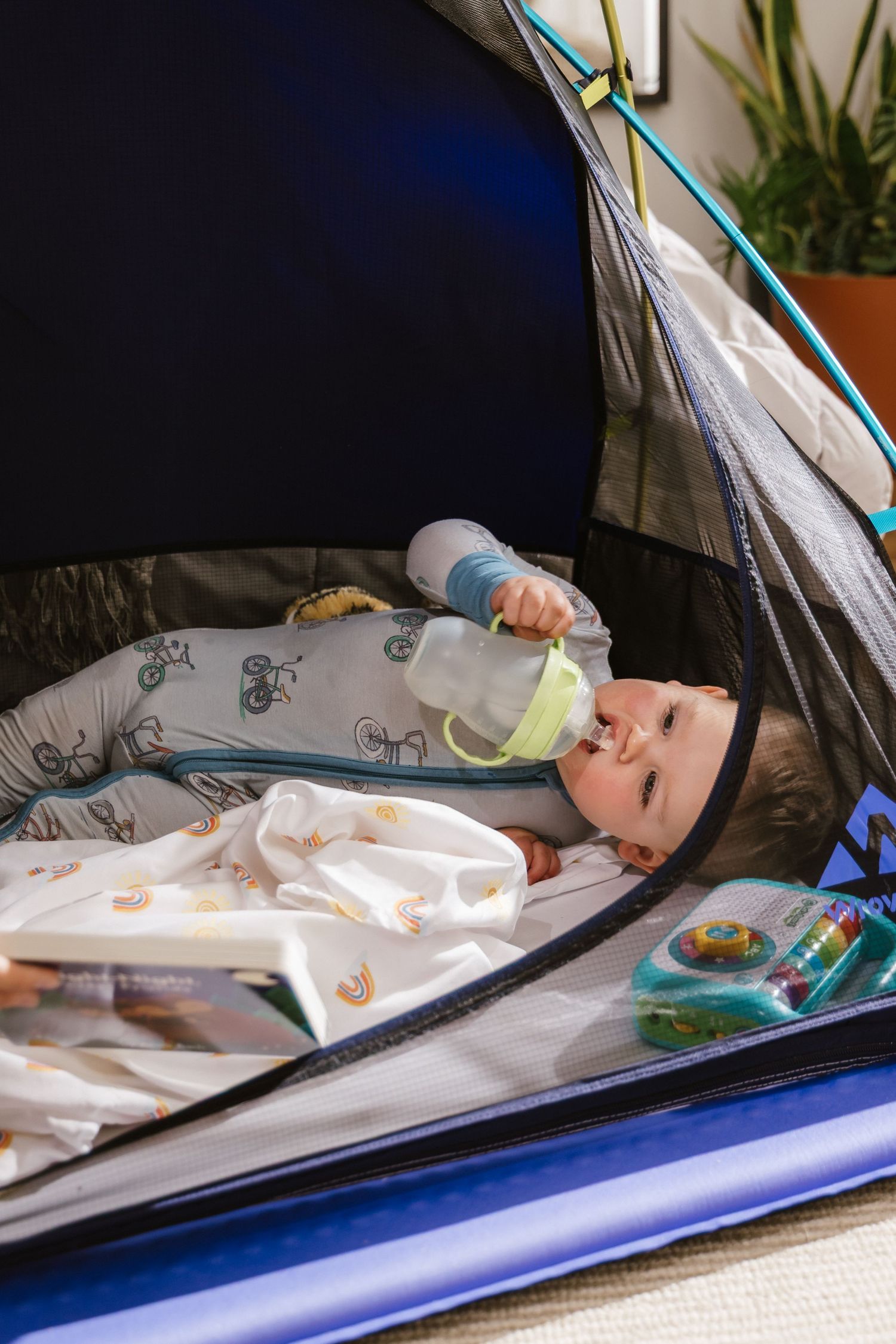 Baby lying in a tent wearing patterned sleepwear while drinking from a bottle.