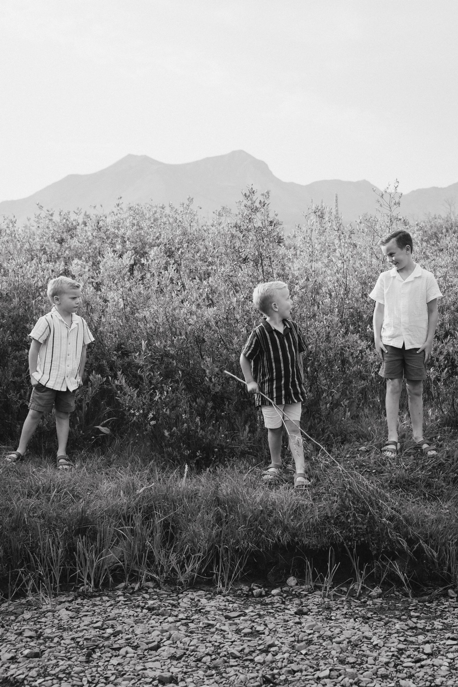 Three boys playing outdoors in a field with mountains in the background, black and white photo.