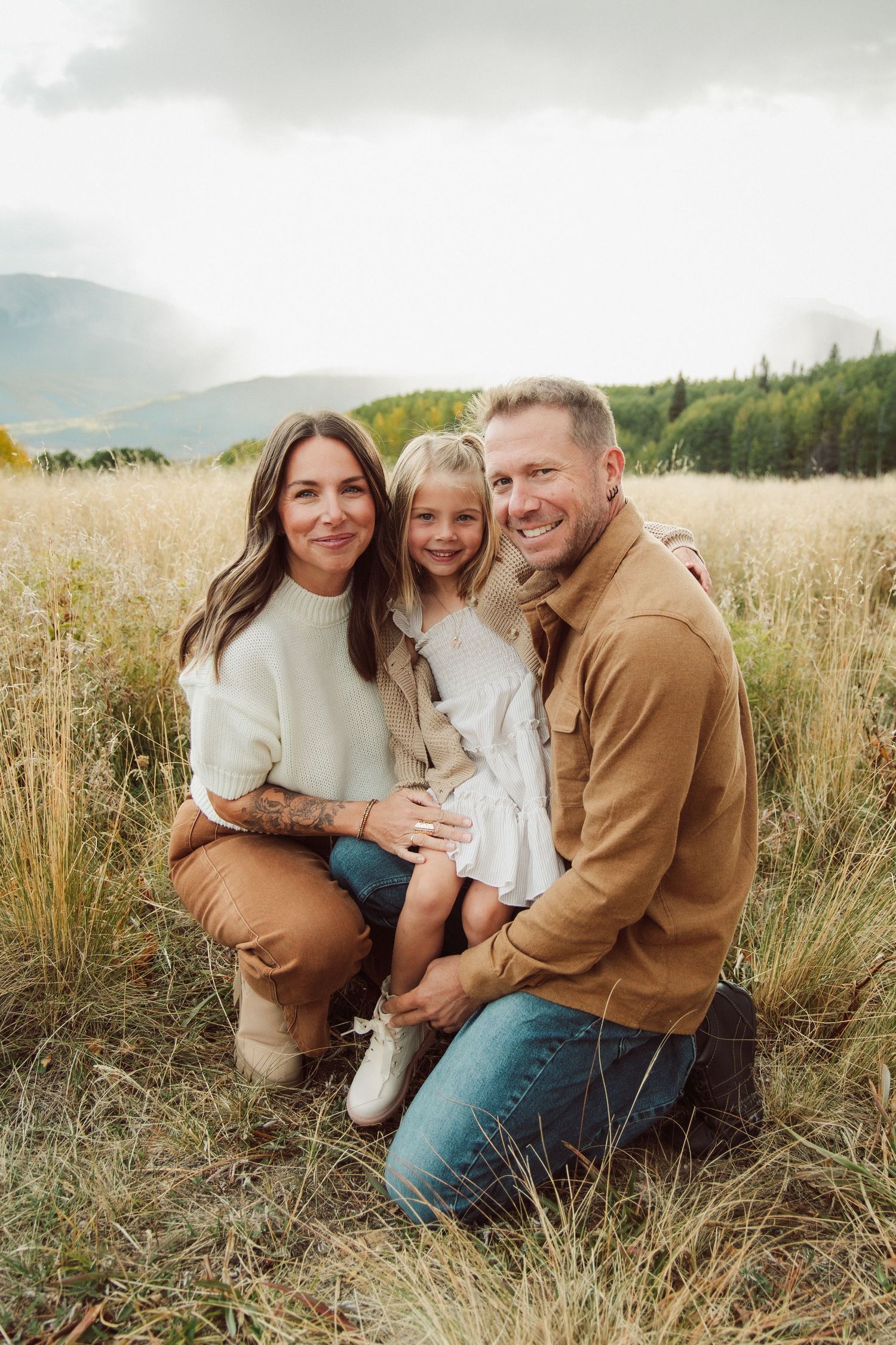 Candid family moments captured in a sun-lit meadow with mountain scenery.