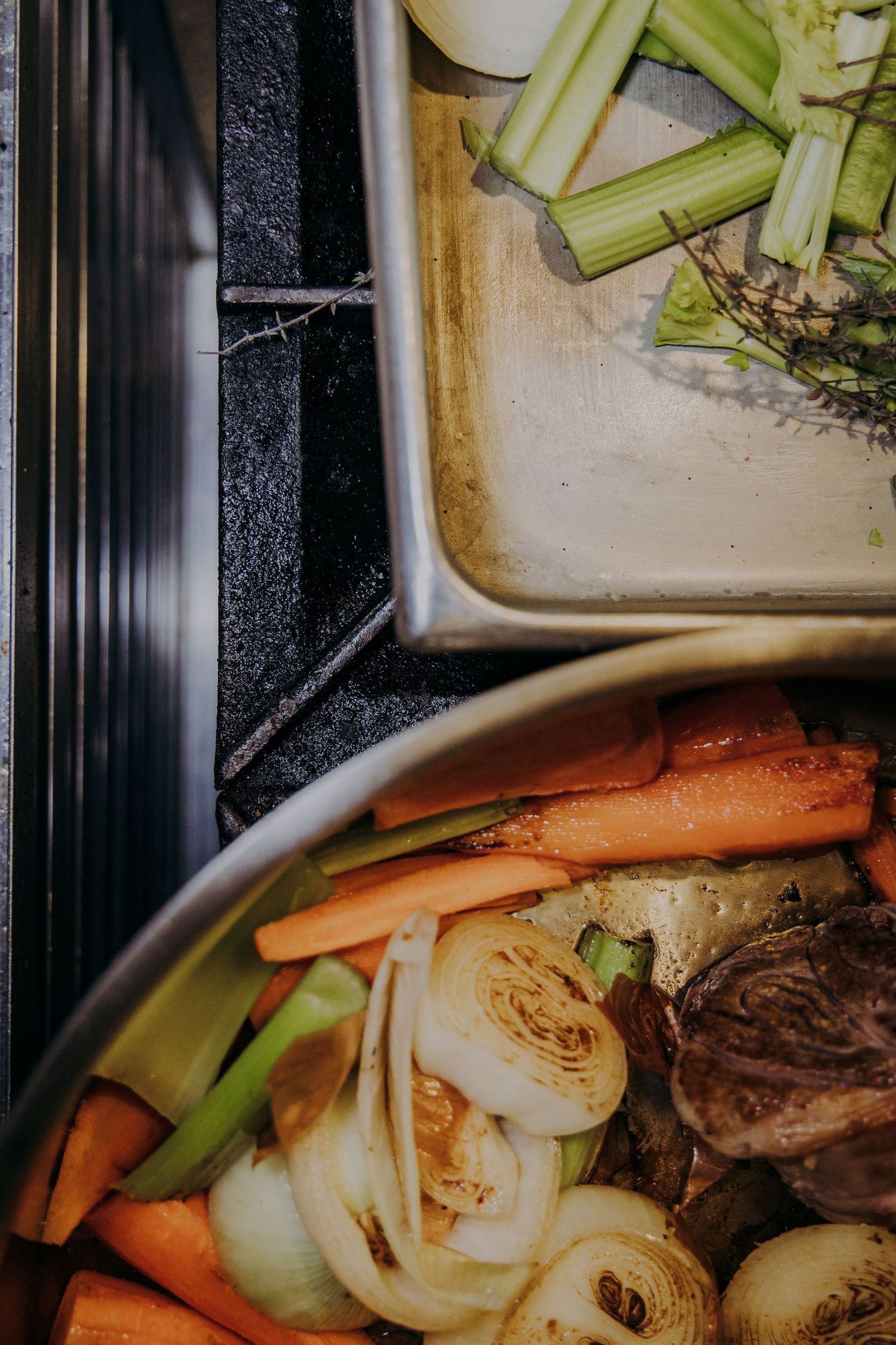 Fresh vegetables including carrots, celery, and onions arranged on a dark baking sheet for roasting.