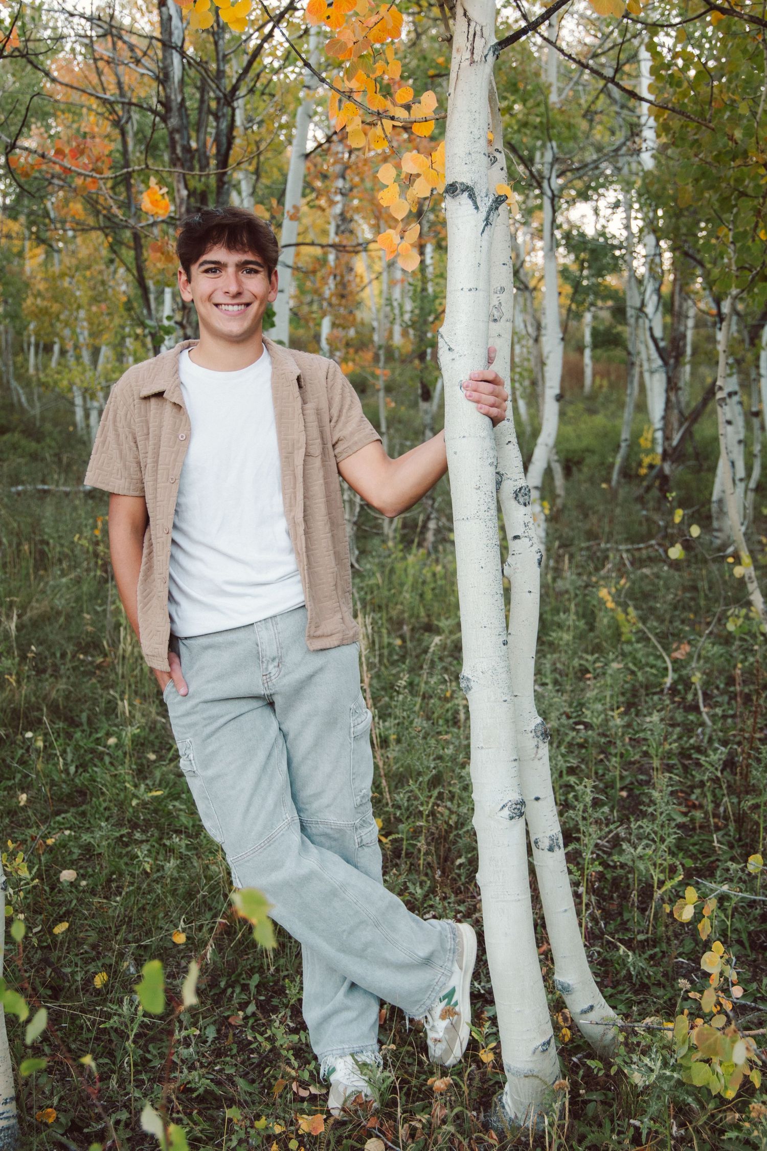 Casual portrait of someone leaning against a white birch tree in an autumn forest.