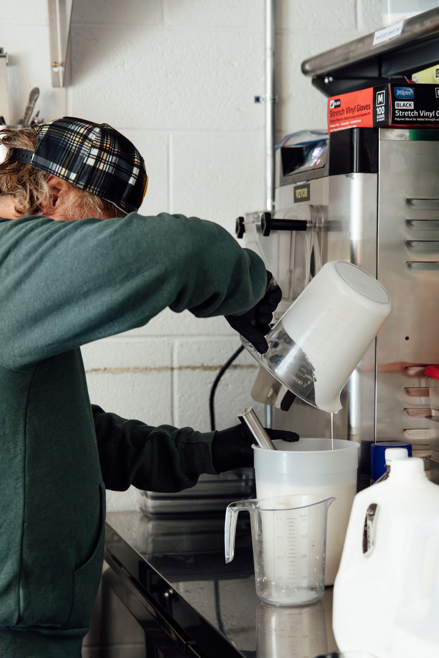 Barista pouring steamed milk into a pitcher using a commercial espresso machine in a professional kitchen.