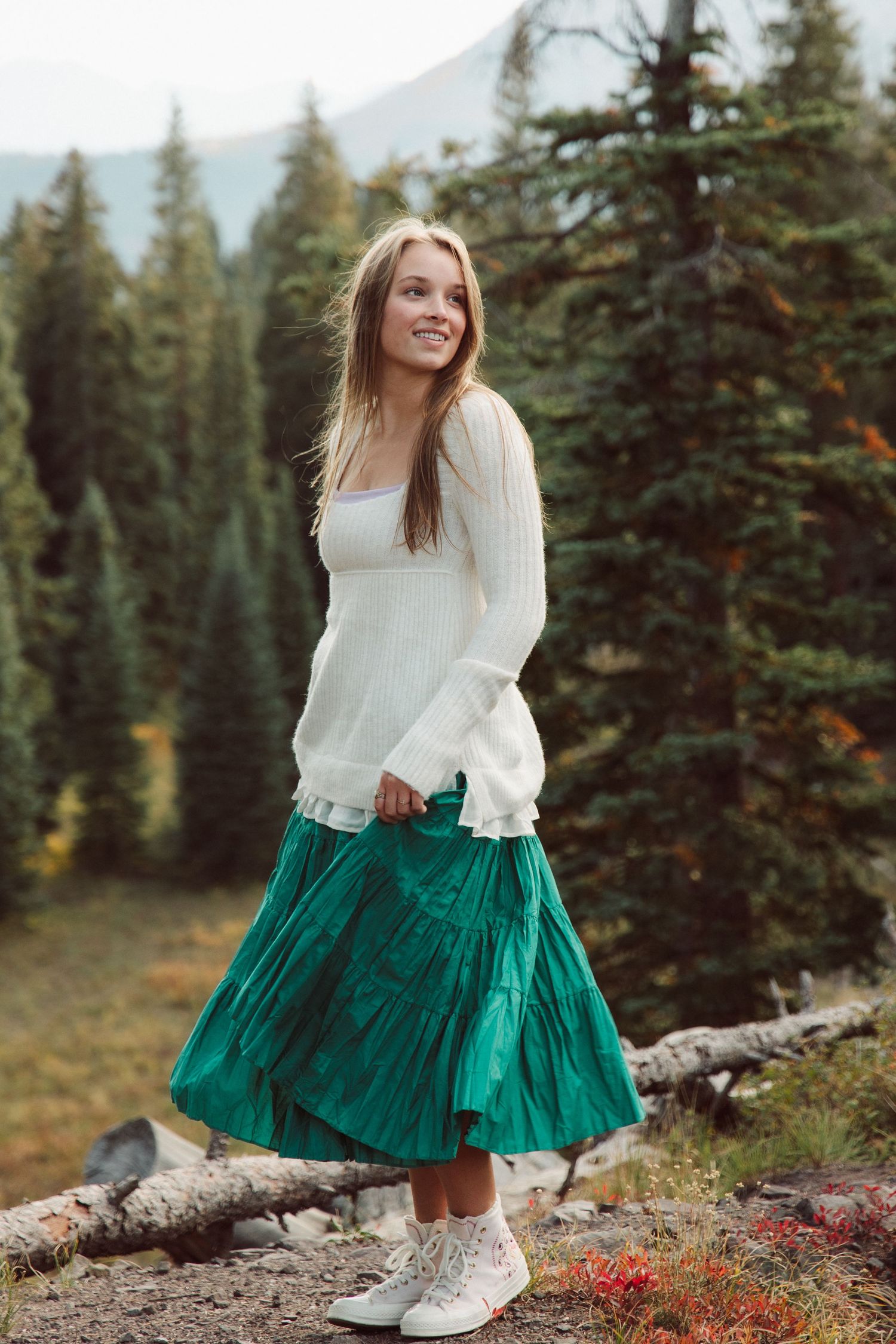 Green tiered skirt and white sweater outfit photographed in mountain forest setting.