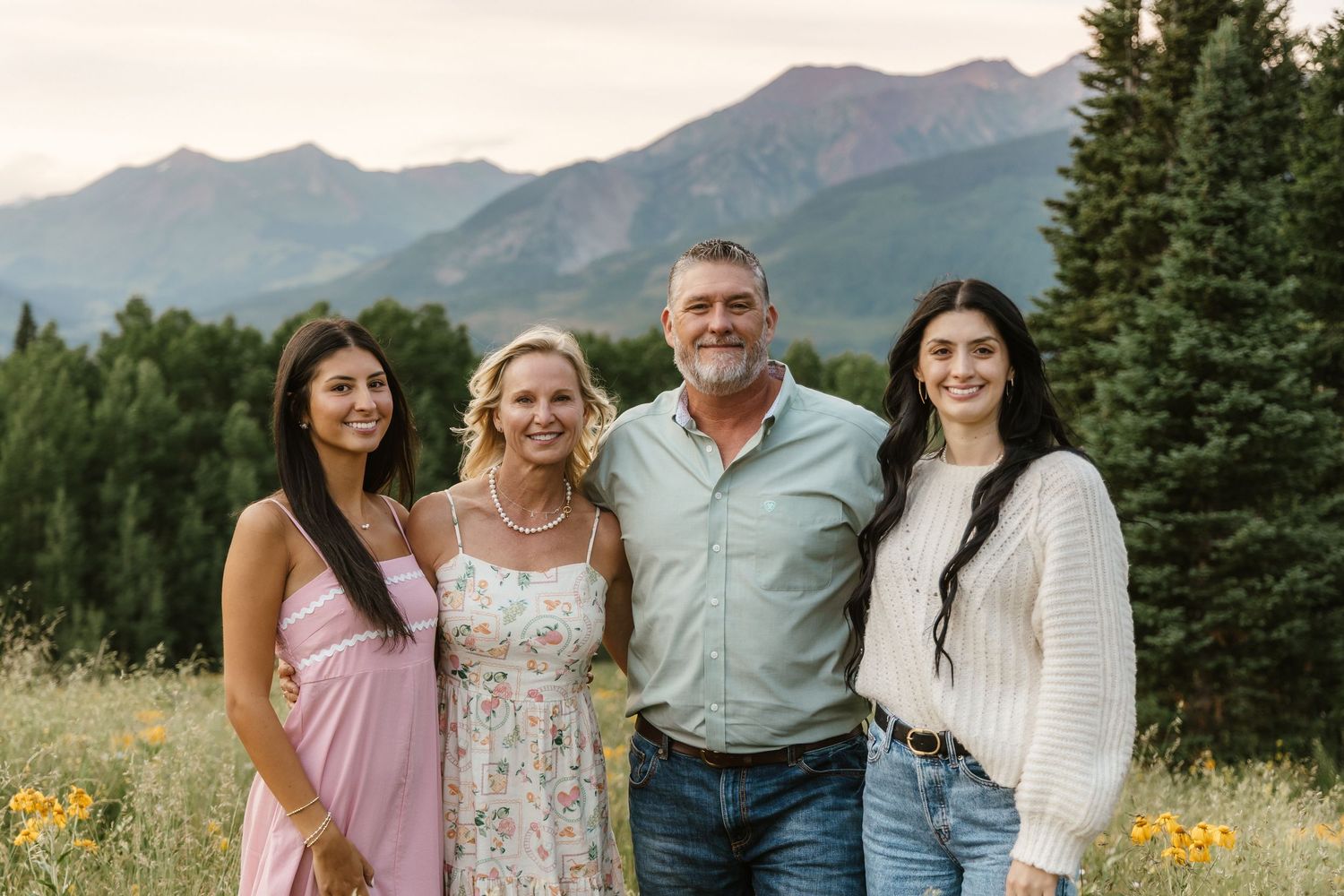 Group of people posing together outdoors with mountains and evergreen trees in the background.