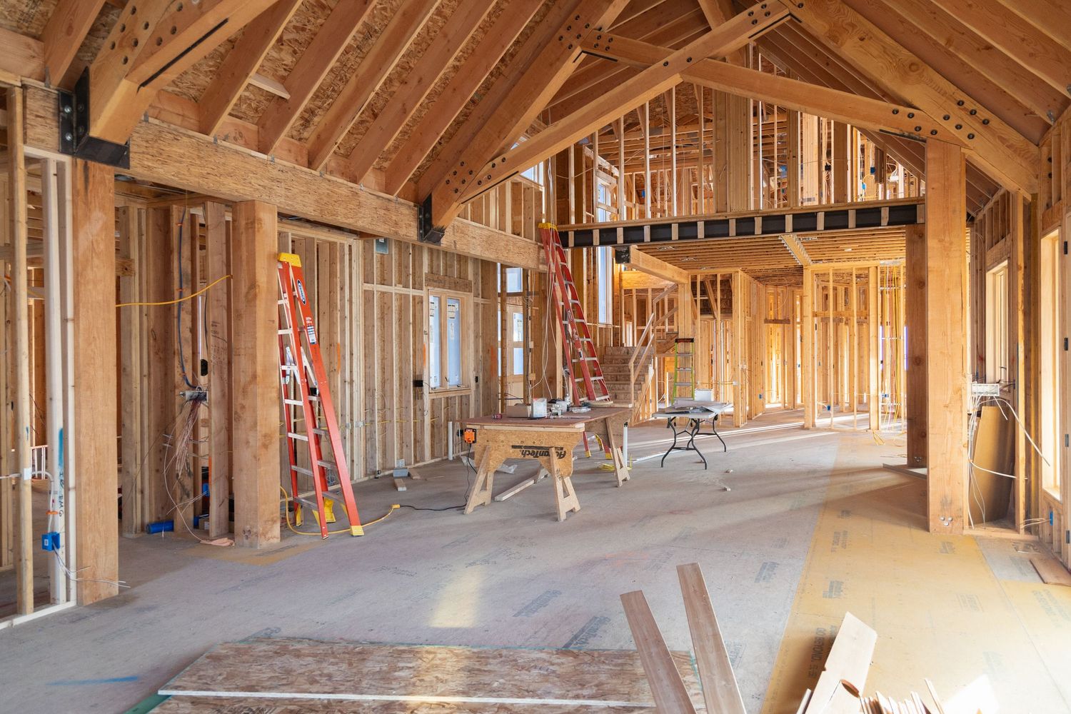 Interior framing of a new home under construction with wooden studs, vaulted ceiling, ladders, and sawhorses on a job site.