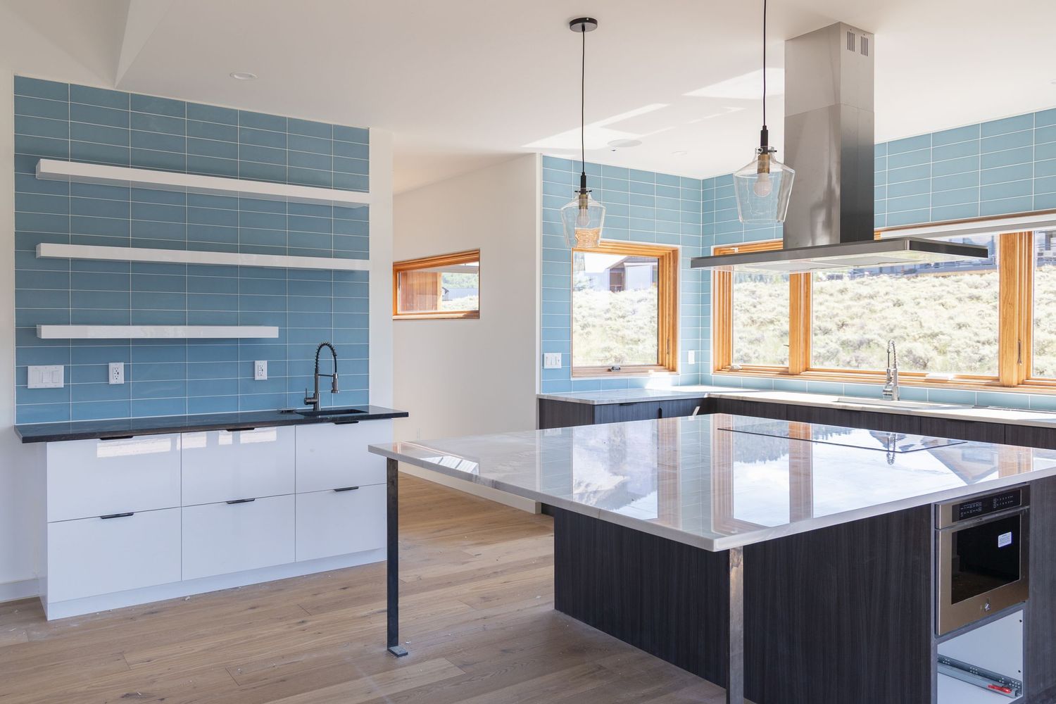 Modern kitchen with blue tile backsplash, white cabinets, dark island, pendant lights, and hardwood floors.