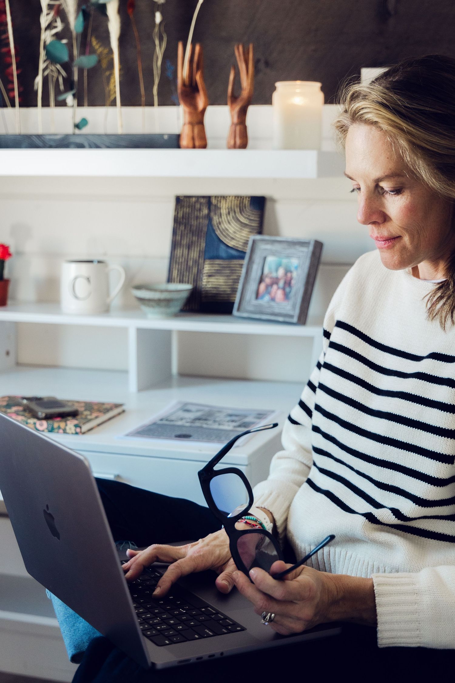 Person in striped shirt working at desk with laptop and office supplies in bright modern workspace.