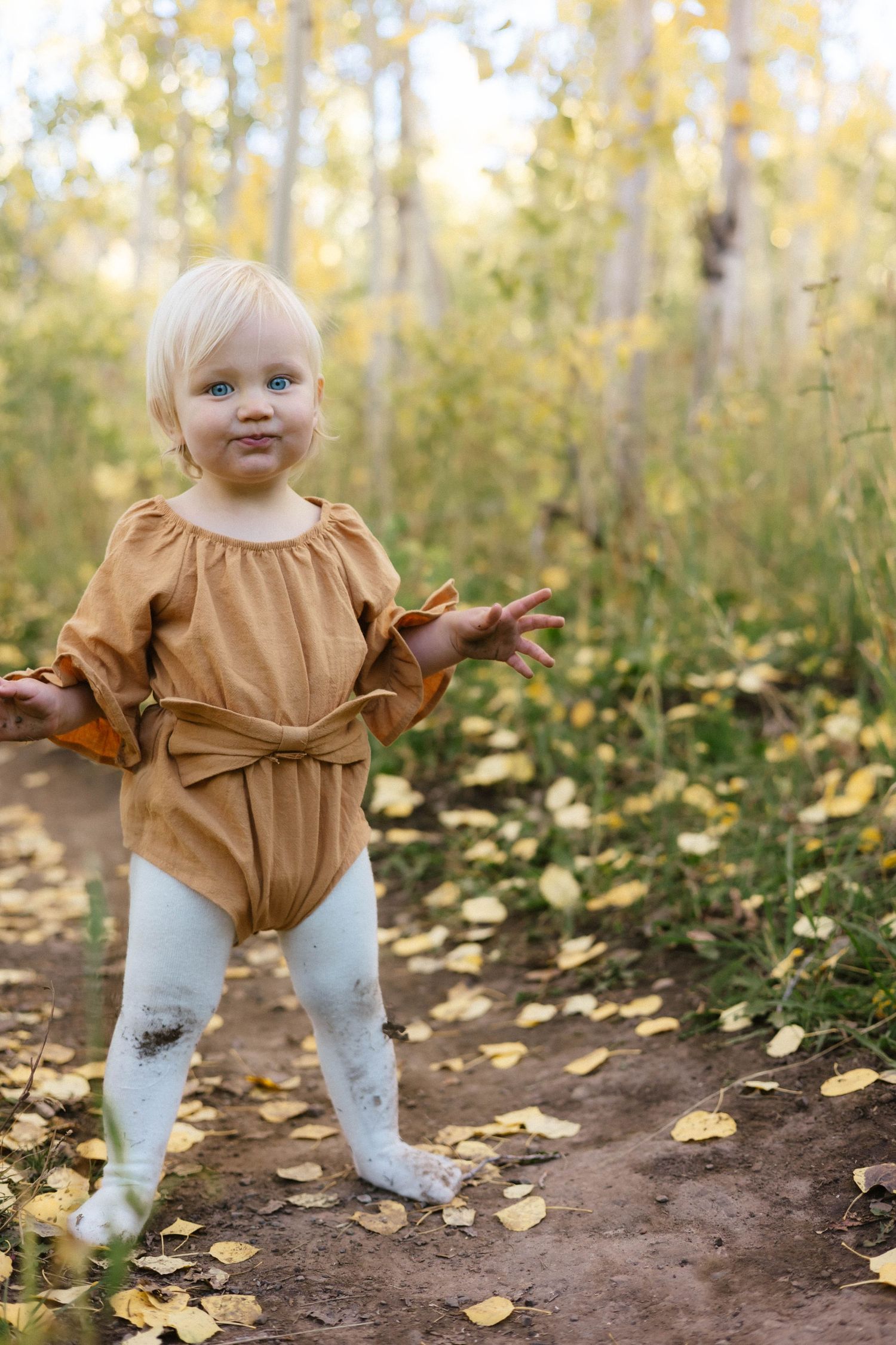 Small child in a brown dress and white tights playing among fallen autumn leaves.