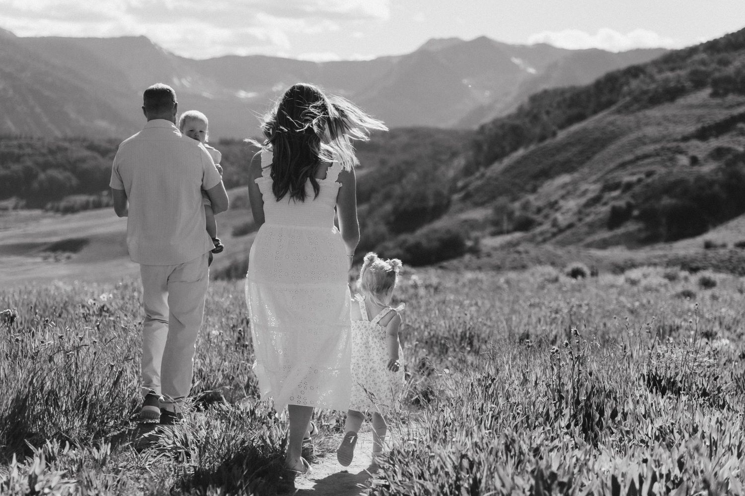 Black and white photo of a family walking through a mountain meadow, parents and children enjoying nature together.