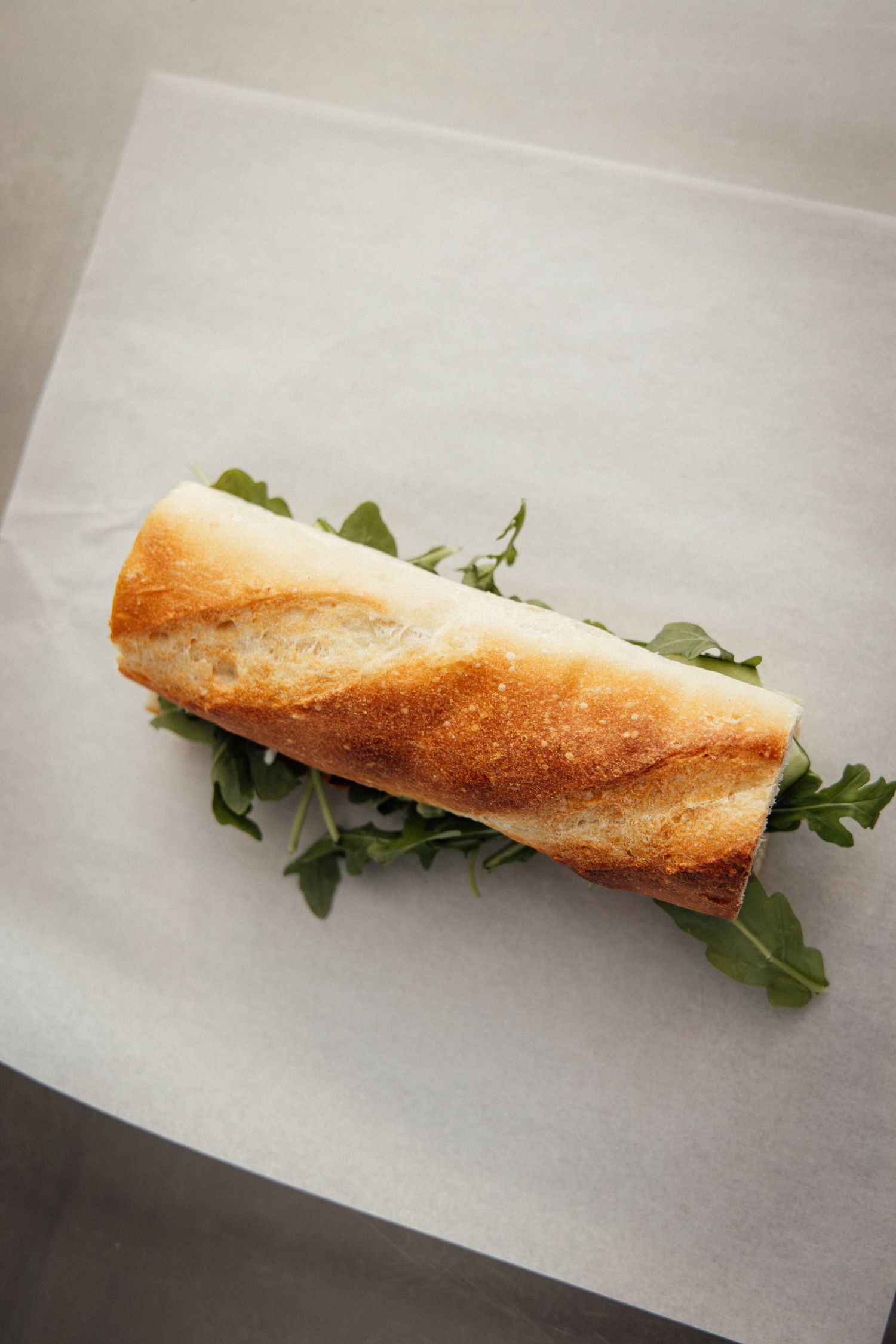 Fresh baguette sandwich filled with arugula on white parchment paper.