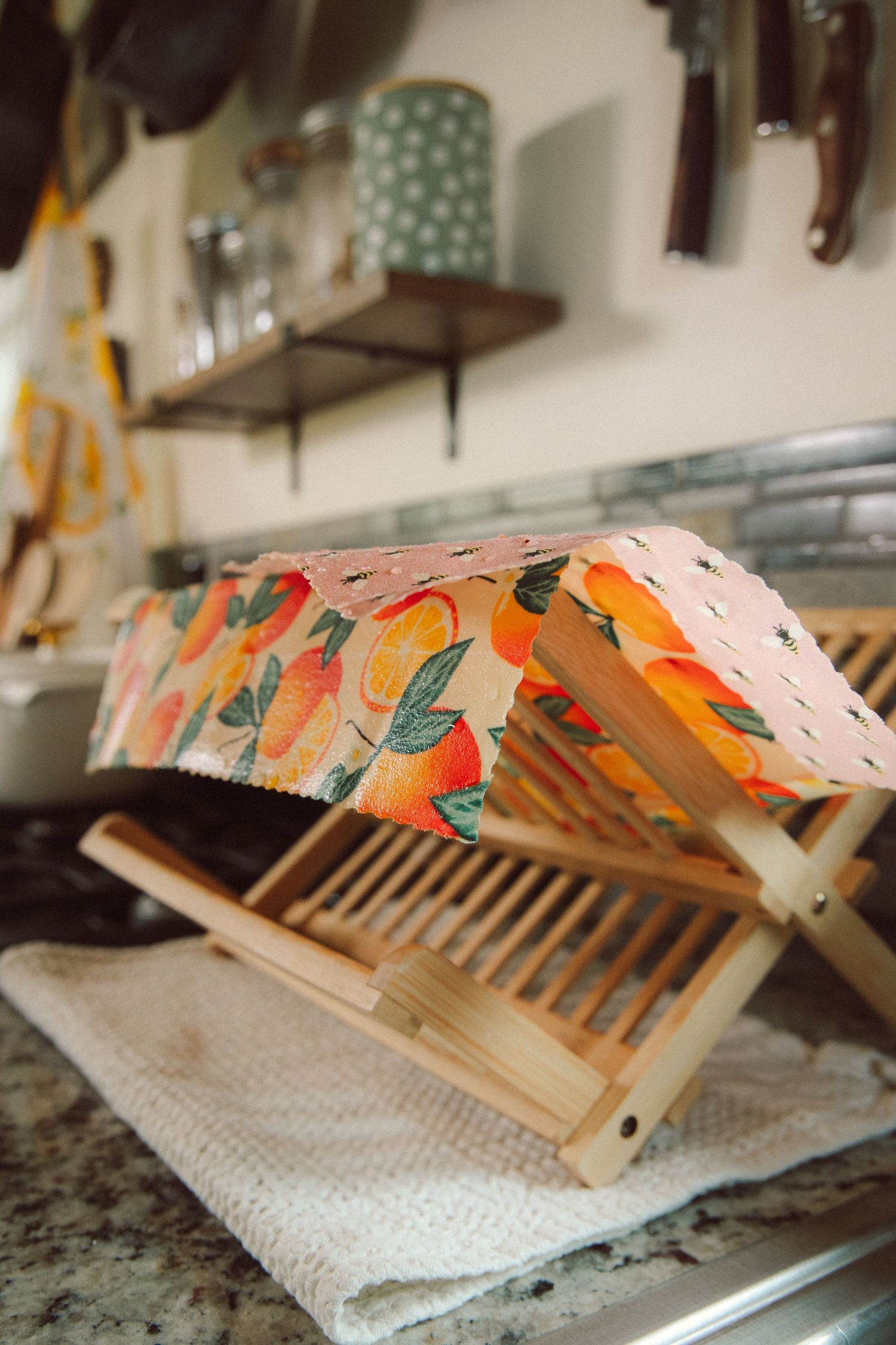 Colorful citrus-patterned dish drying rack with wooden slats sits on a marble countertop in a kitchen.