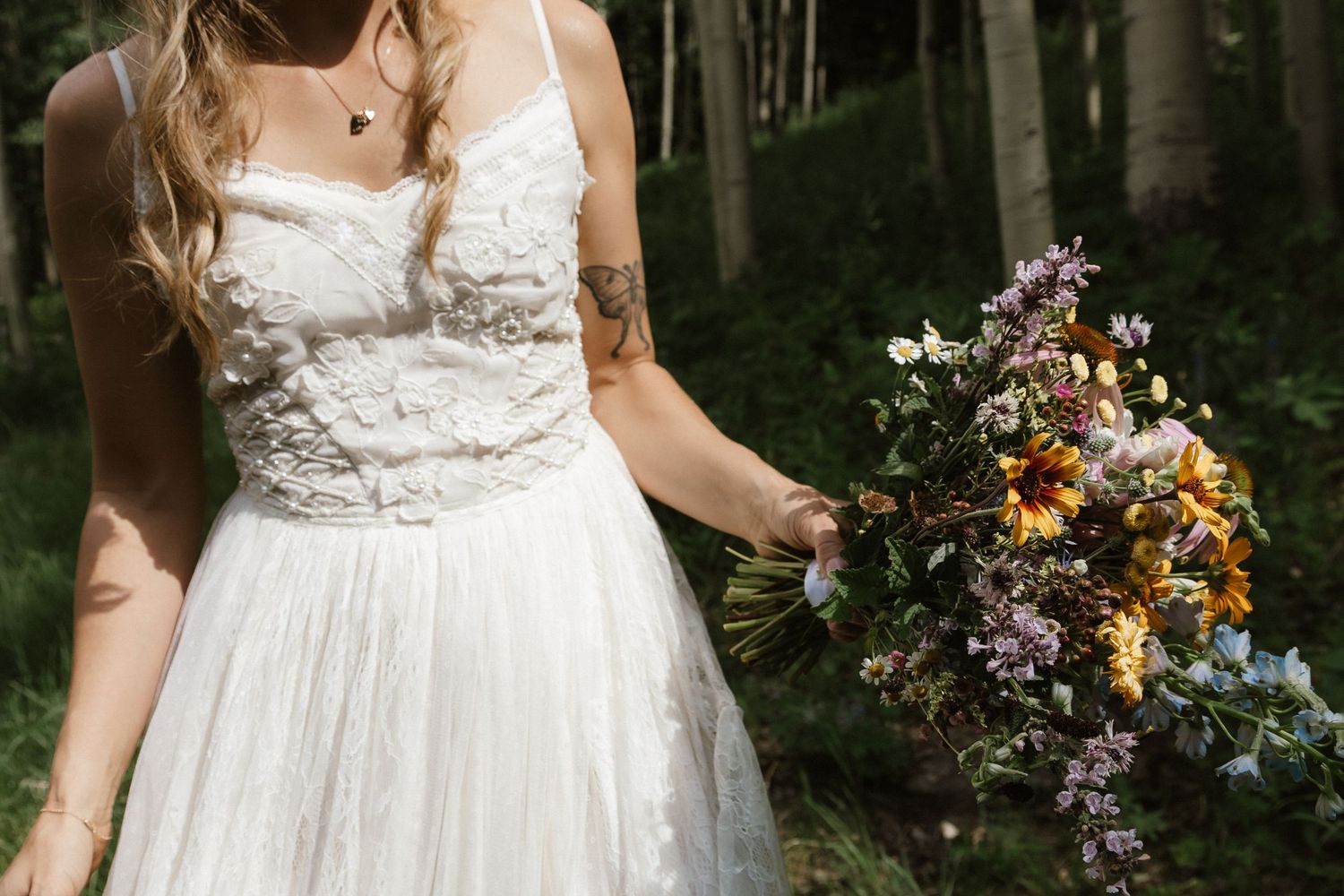 Wedding dress details with delicate lace and floral elements in a forest setting.