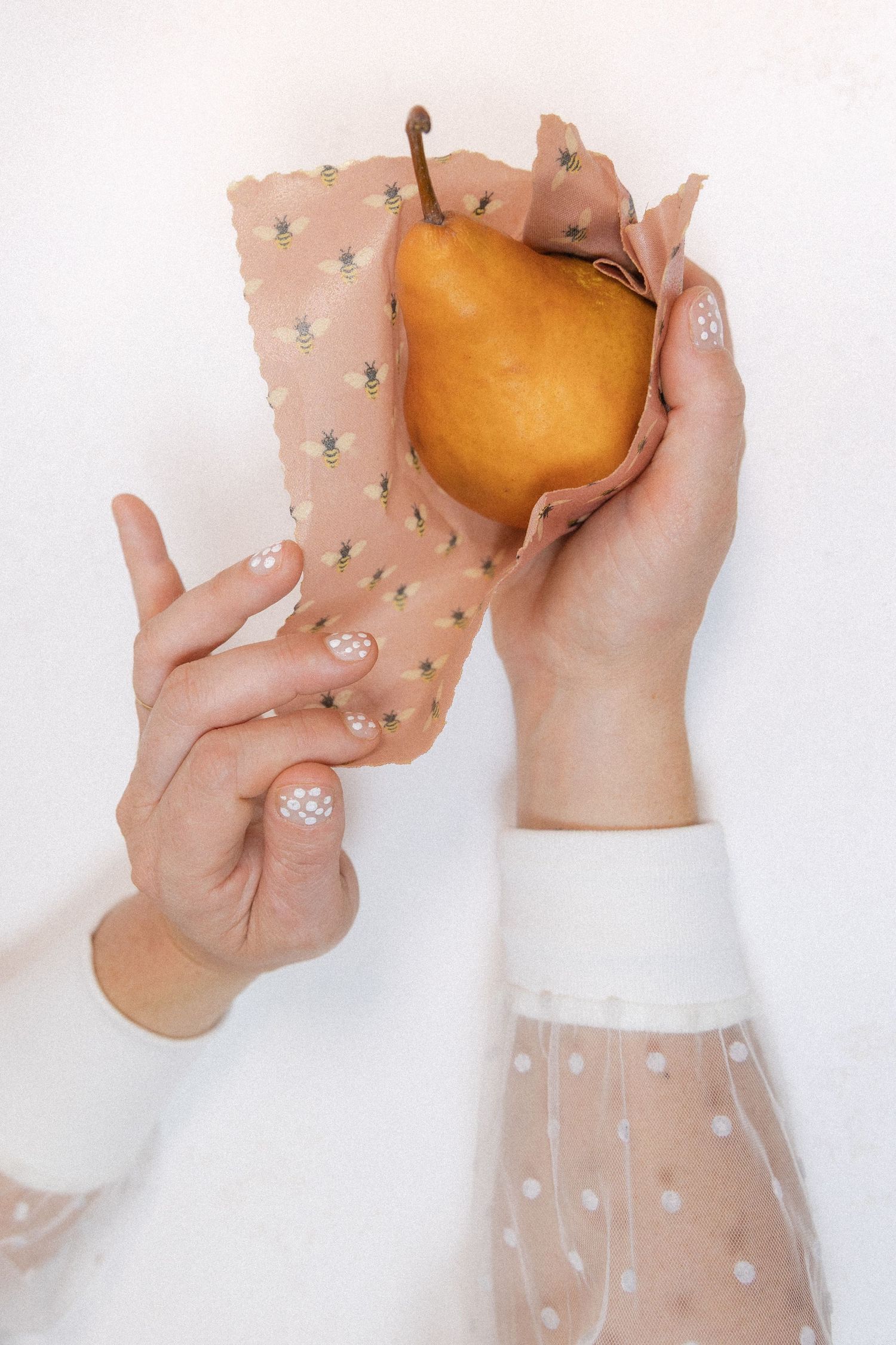 Hands holding a golden pear wrapped in polka dot tissue paper against a white background.