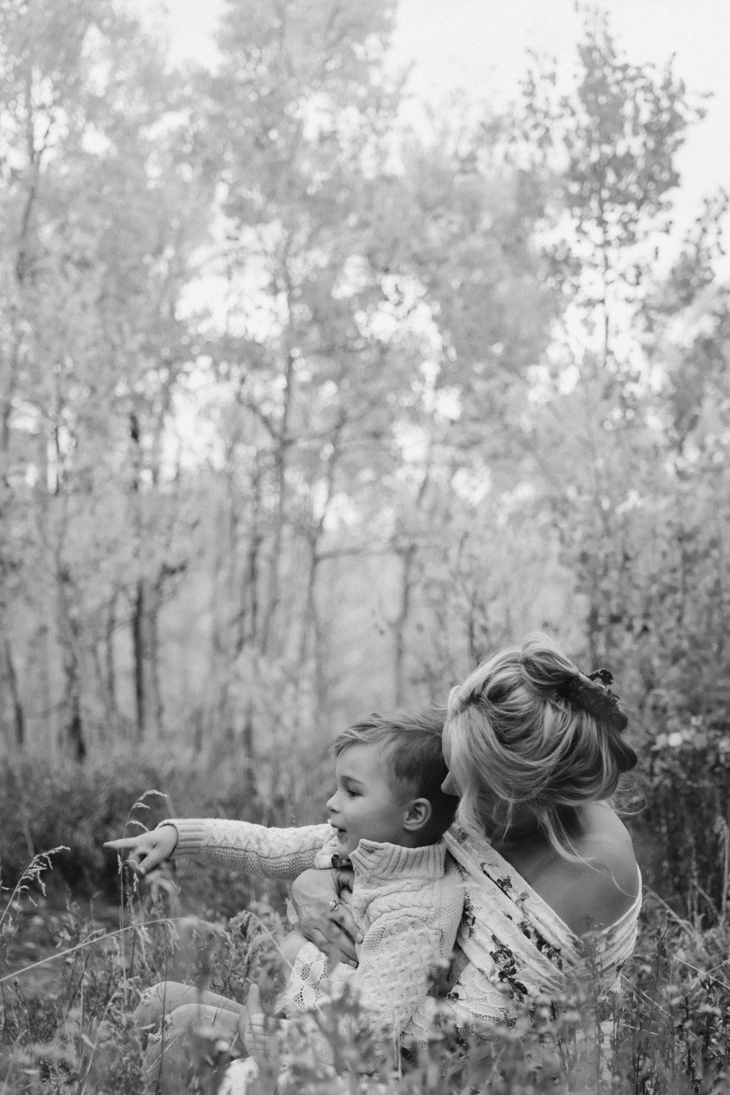 A tender black and white moment captured in nature as two figures sit together among wildflowers and trees. Crested Butte