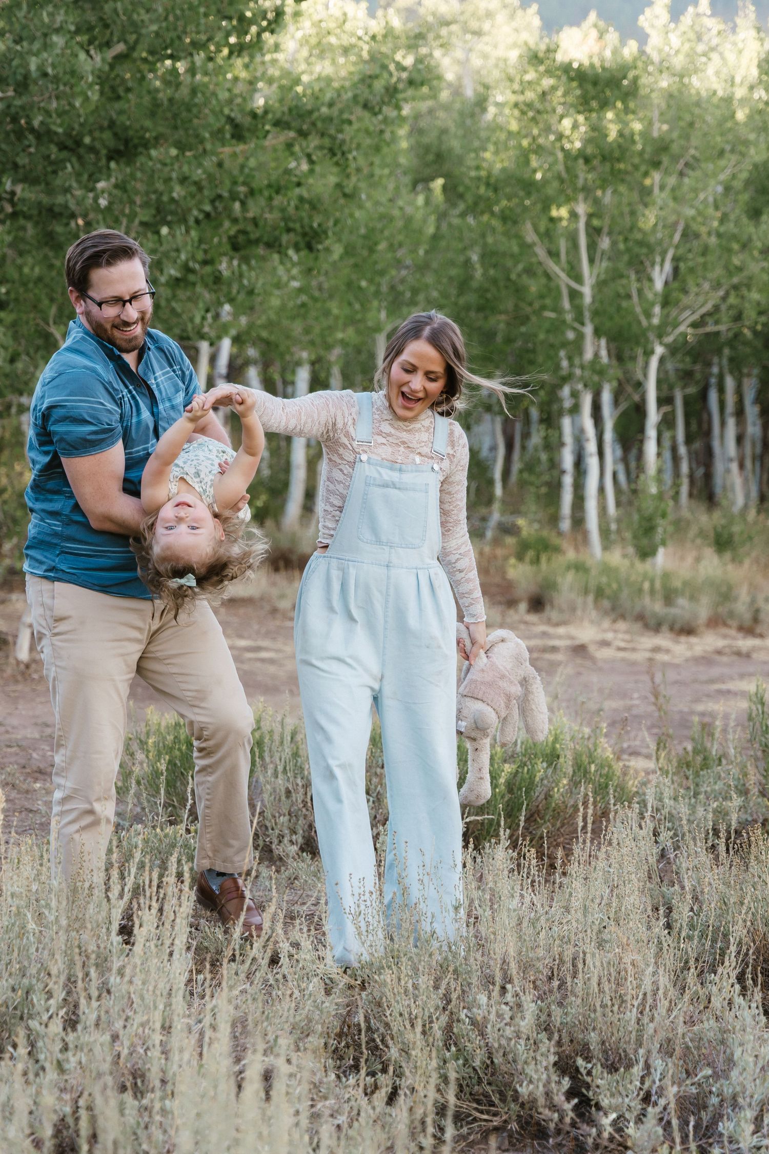 Family playing and laughing together in a field with aspen trees in the background.
