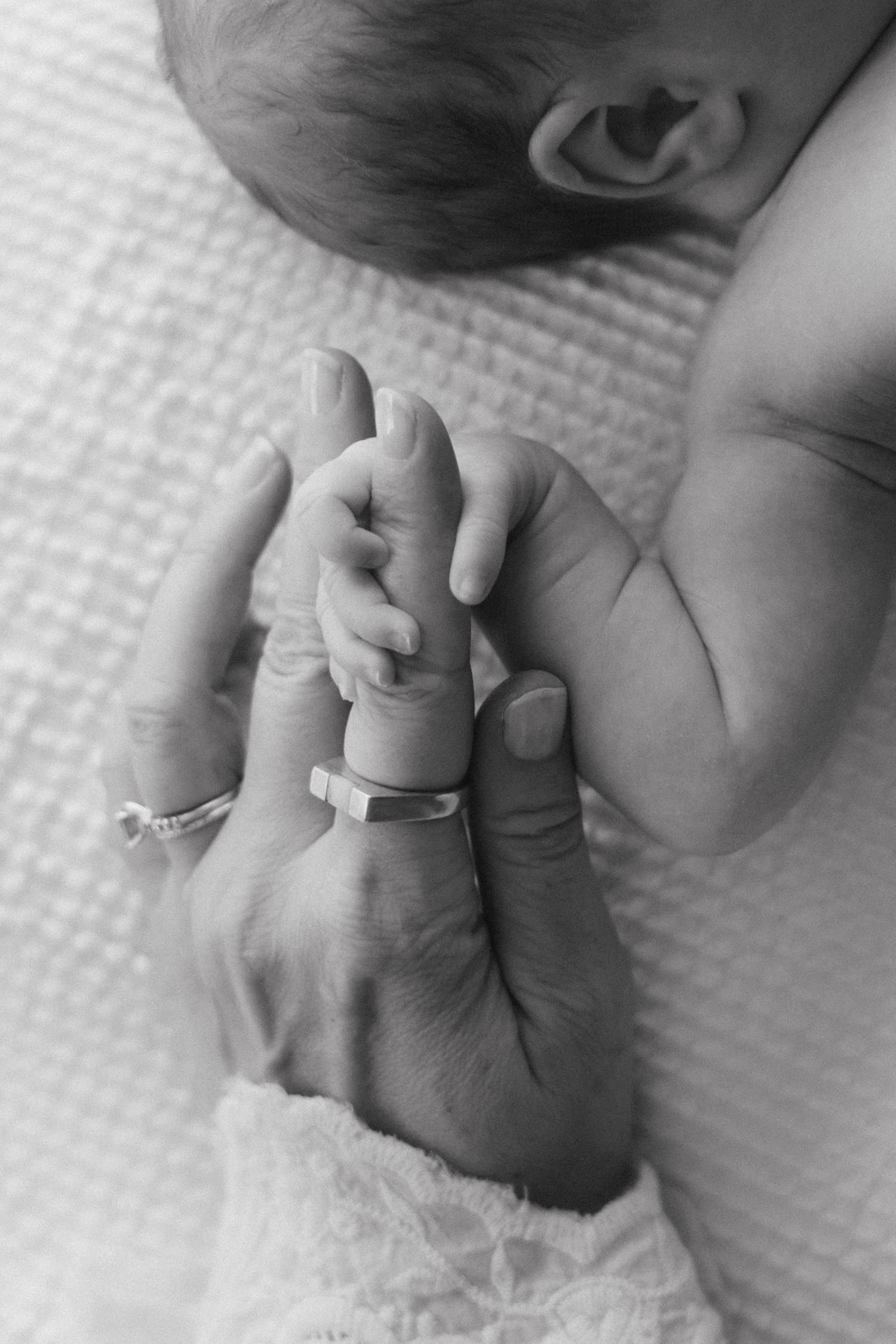 A tender black and white image of a tiny baby's hand grasping an adult's finger with rings.