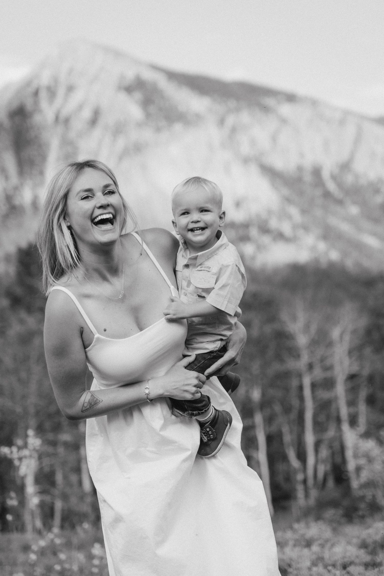 A joyful black and white portrait of parent and child laughing together against a scenic mountain backdrop.