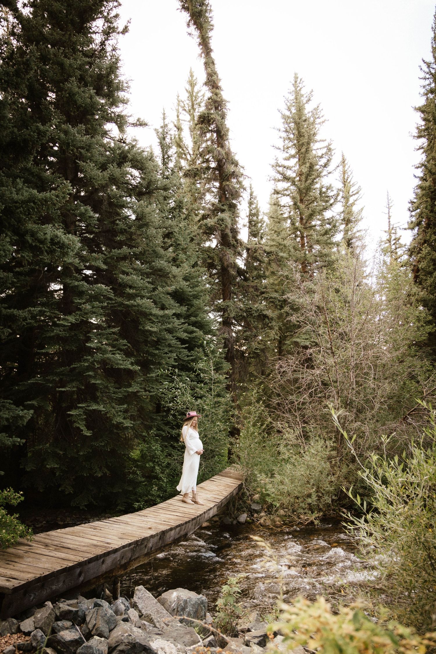 Maternity photography session in Crested Butte, Colorado woman on bridge by the river.
