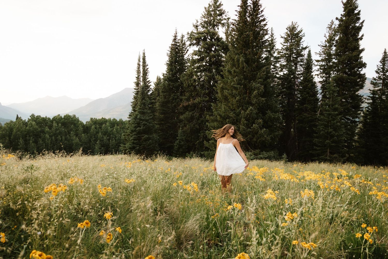 Senior photography session in Crested Butte, Colorado twirling in wildflowers with mountain views and pine trees.