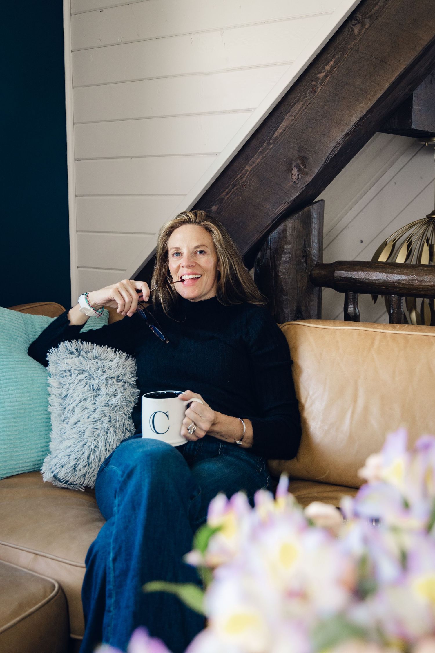 Person relaxes on a tan leather couch with a coffee mug while soft purple flowers bloom in the foreground.