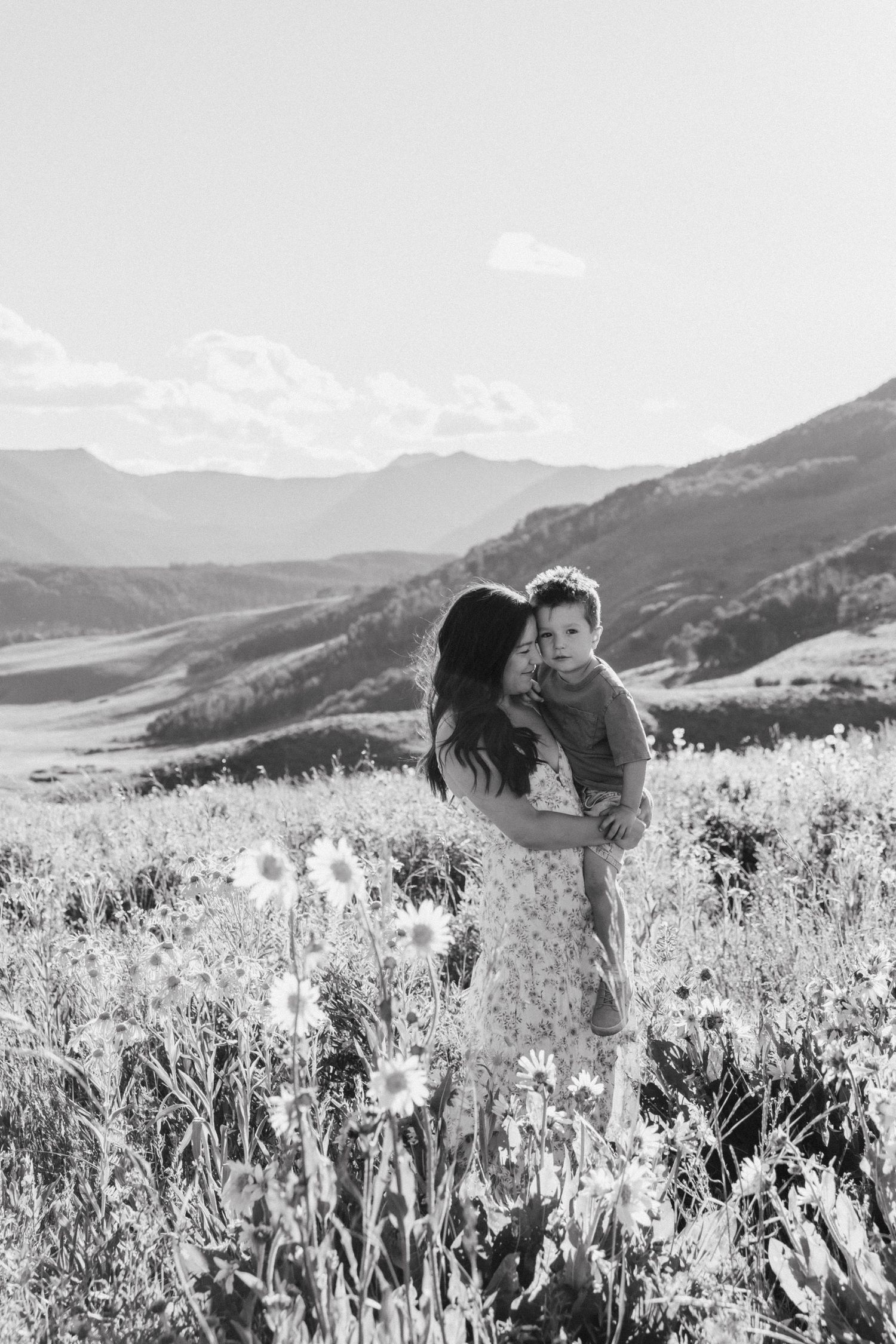 A sweet embrace amidst wildflowers with mountain views in black and white photography.