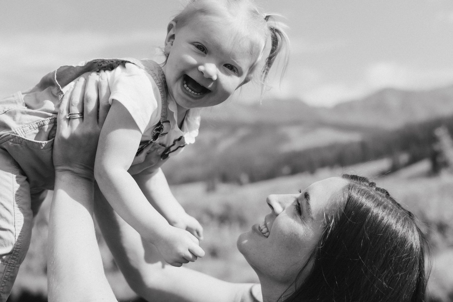 A joyful black and white moment captured between parent and child against a mountain backdrop.