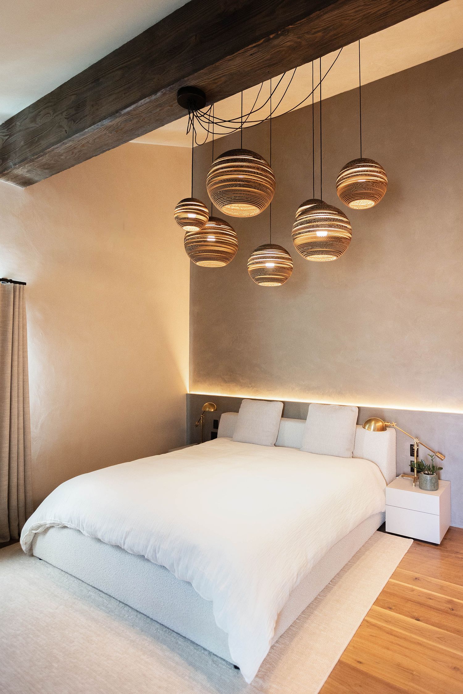 Modern bedroom with white bedding, wooden beam ceiling, and hanging wicker pendant lights above a low-profile bed.