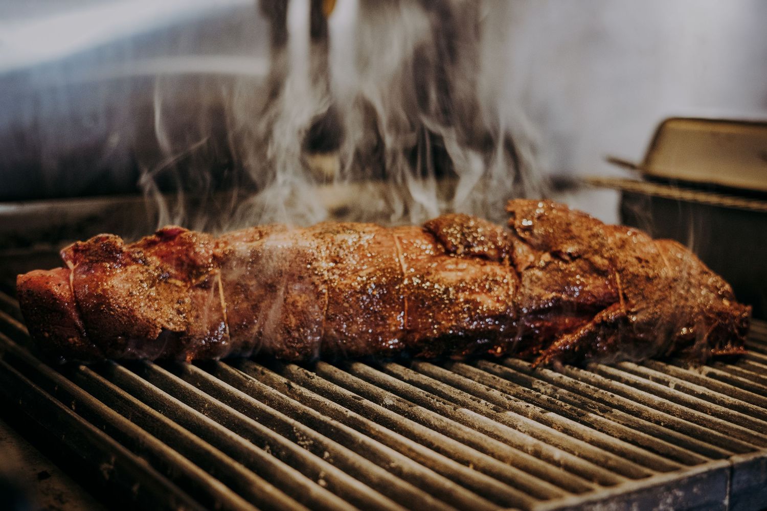 Juicy meat being grilled on hot barbecue grates with rising smoke and flames in the background.
