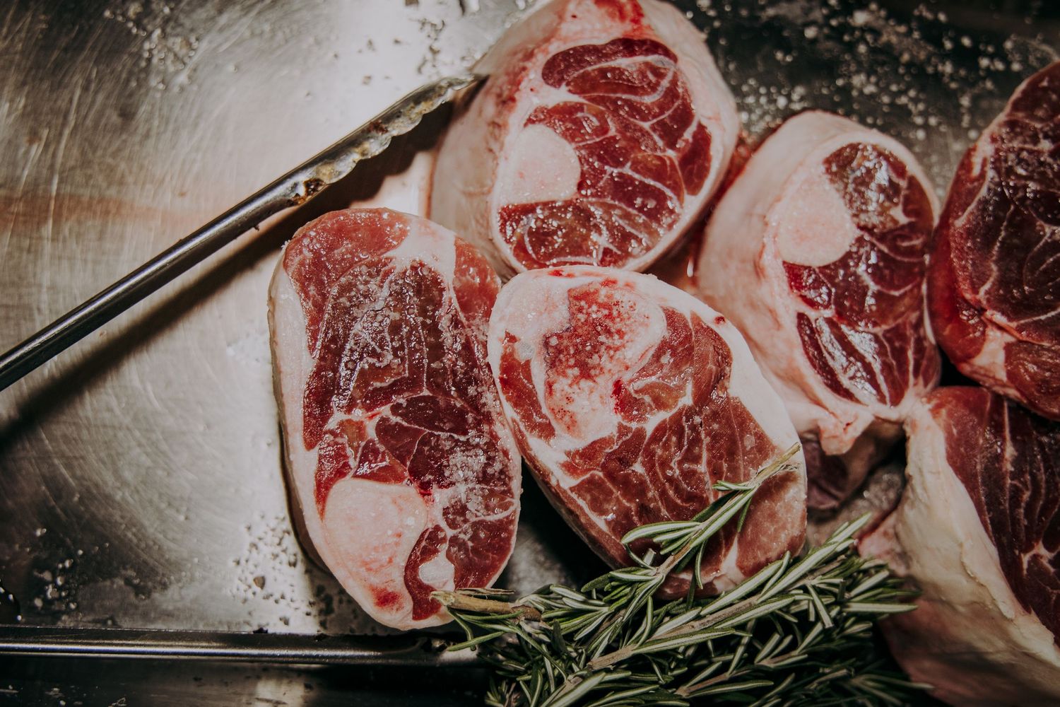 Raw T-bone steaks with fresh rosemary sprigs arranged on a rustic wooden cutting board.