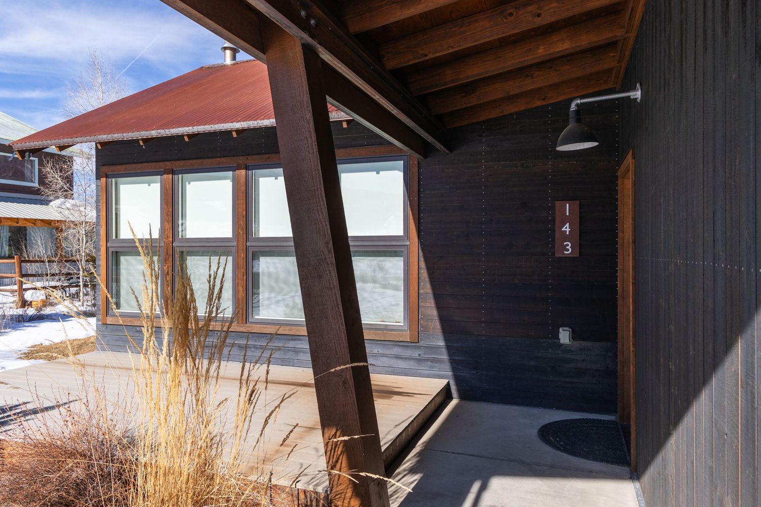 Outdoor shower area on dark wood exterior wall with timber frame accents, snow-covered mountain landscape in background.